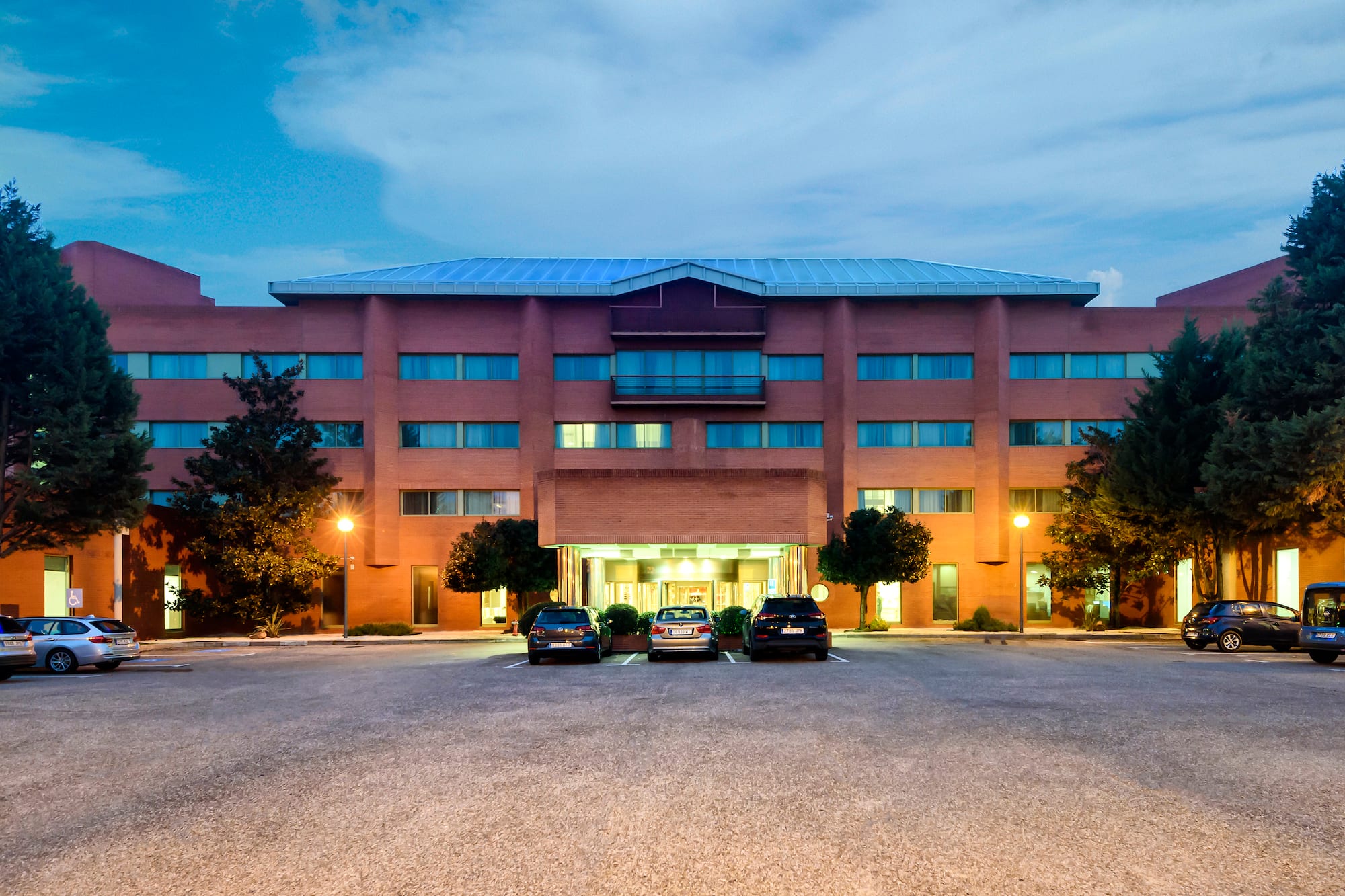 Modern brick hotel building at dusk with parked cars in front of the entrance.