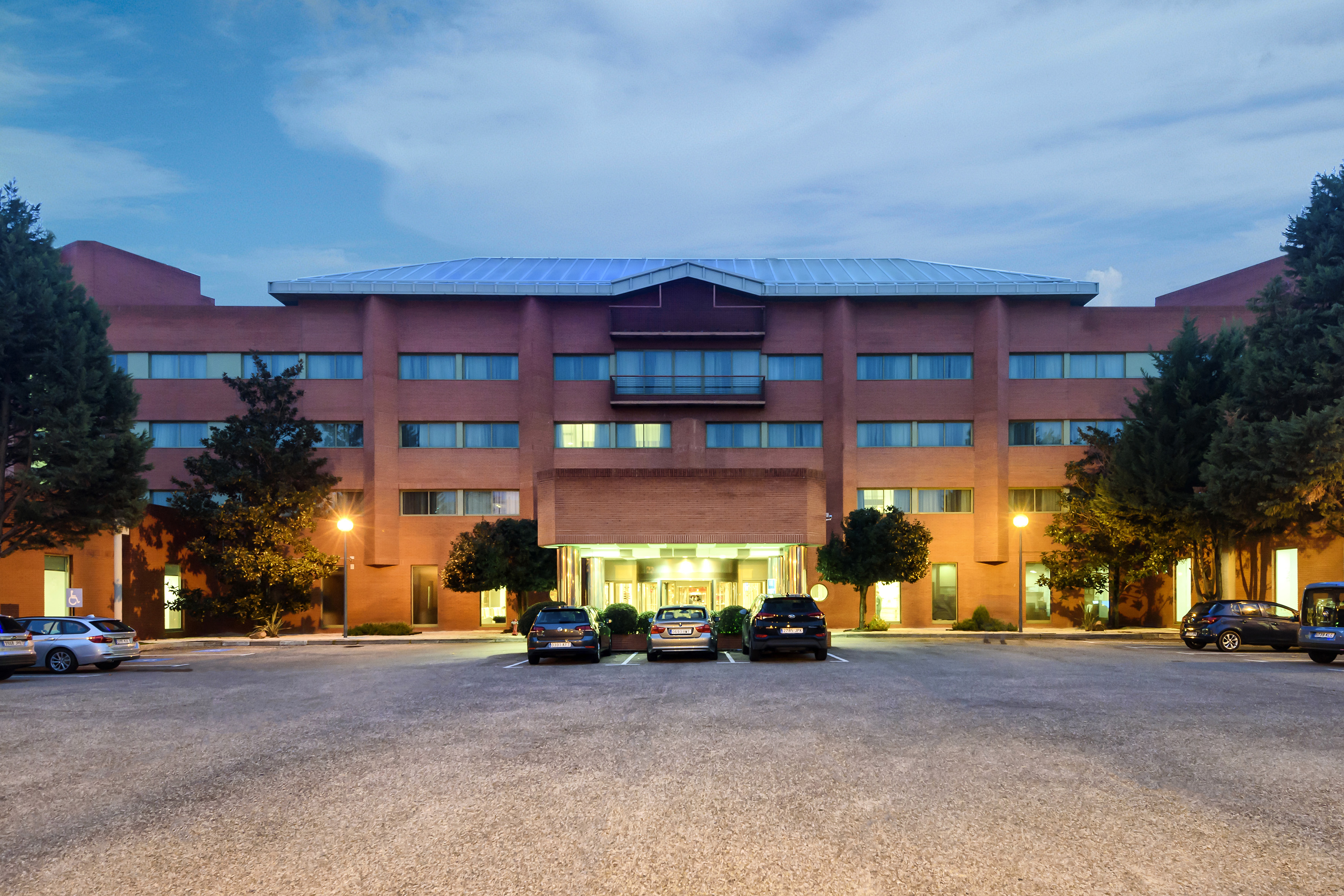 Modern brick hotel building at dusk with parked cars in front of the entrance.