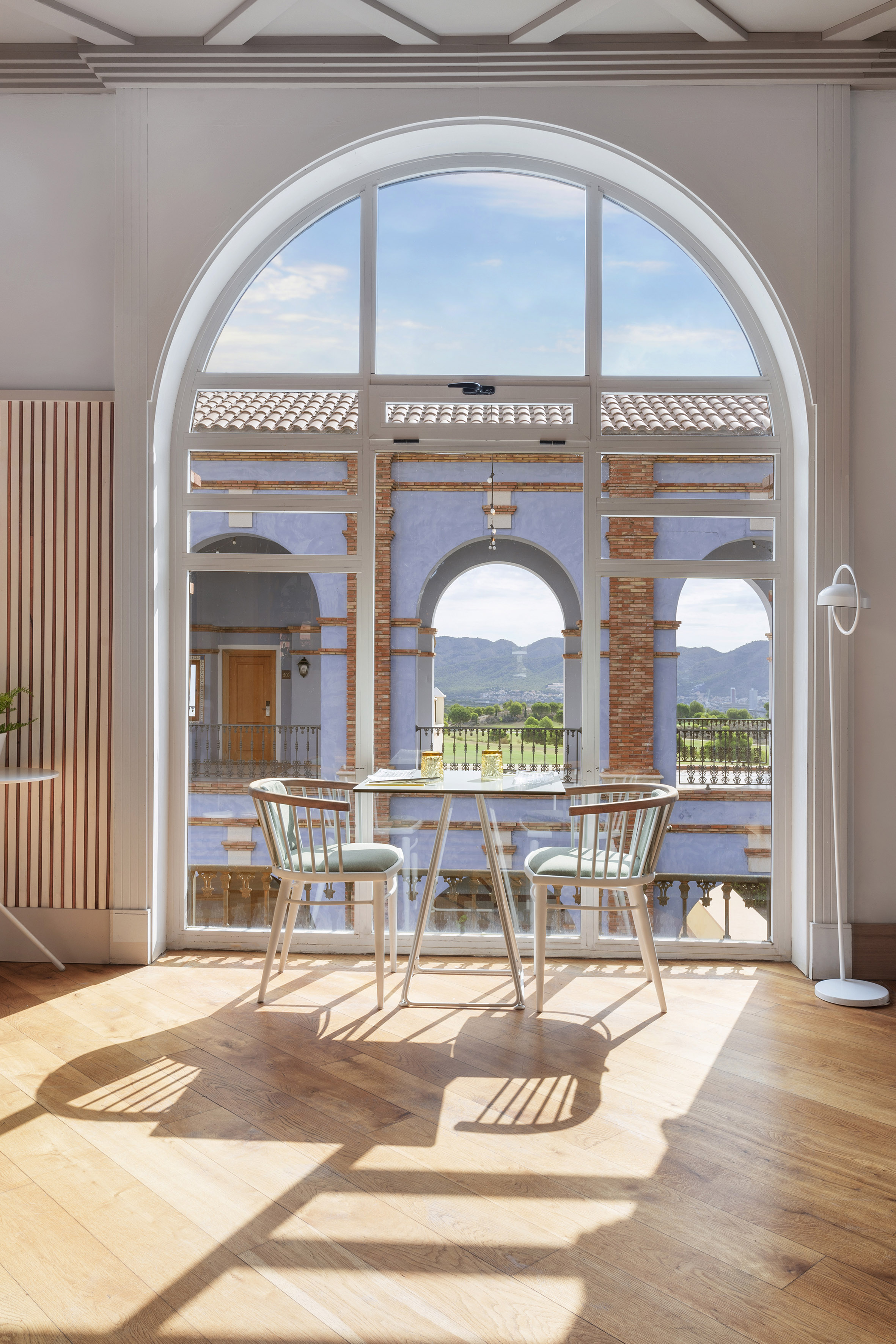Arched window interior with dining table, chairs, and scenic mountain view.