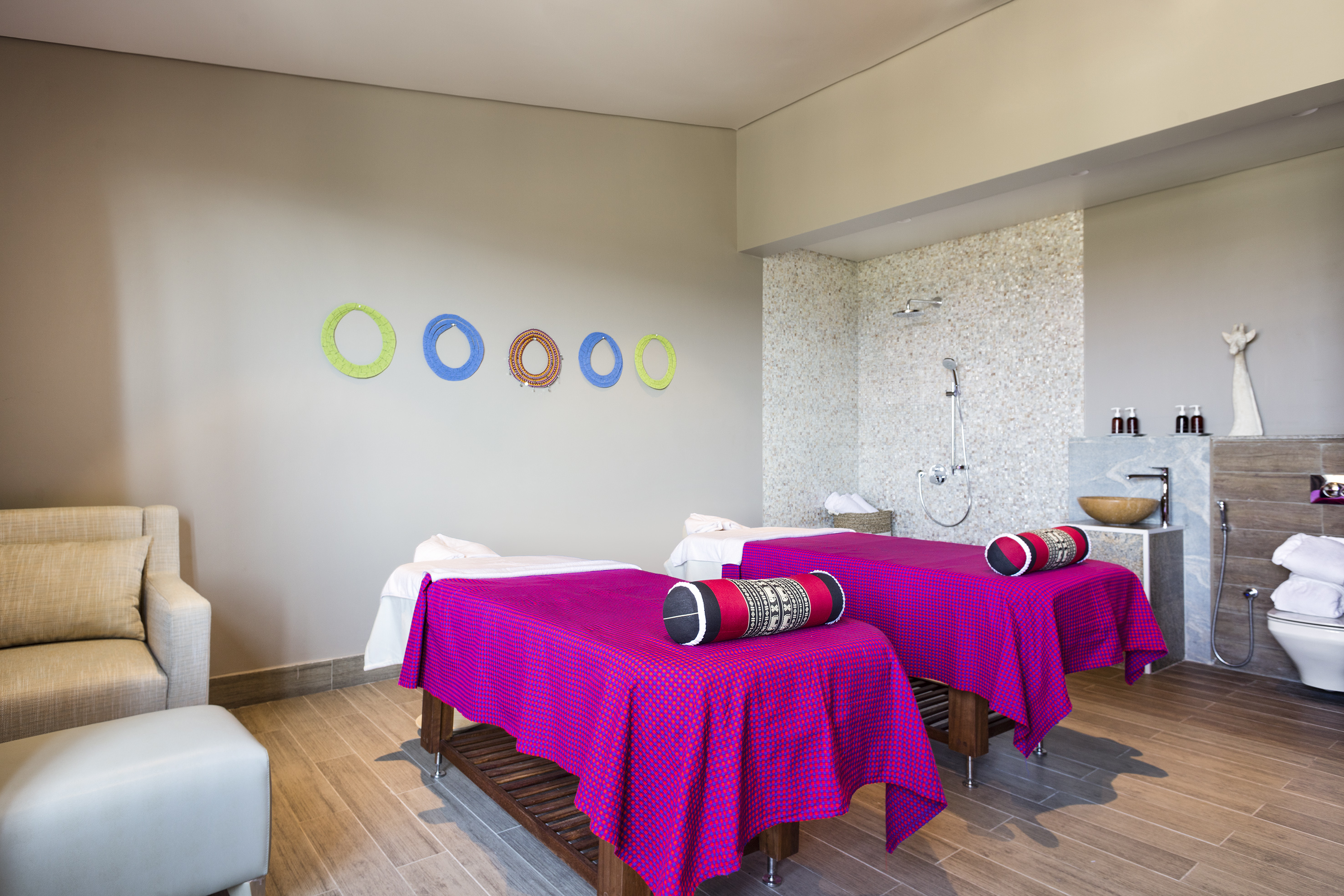 Spa room with two massage beds, magenta throws, modern shower, and colorful rings.