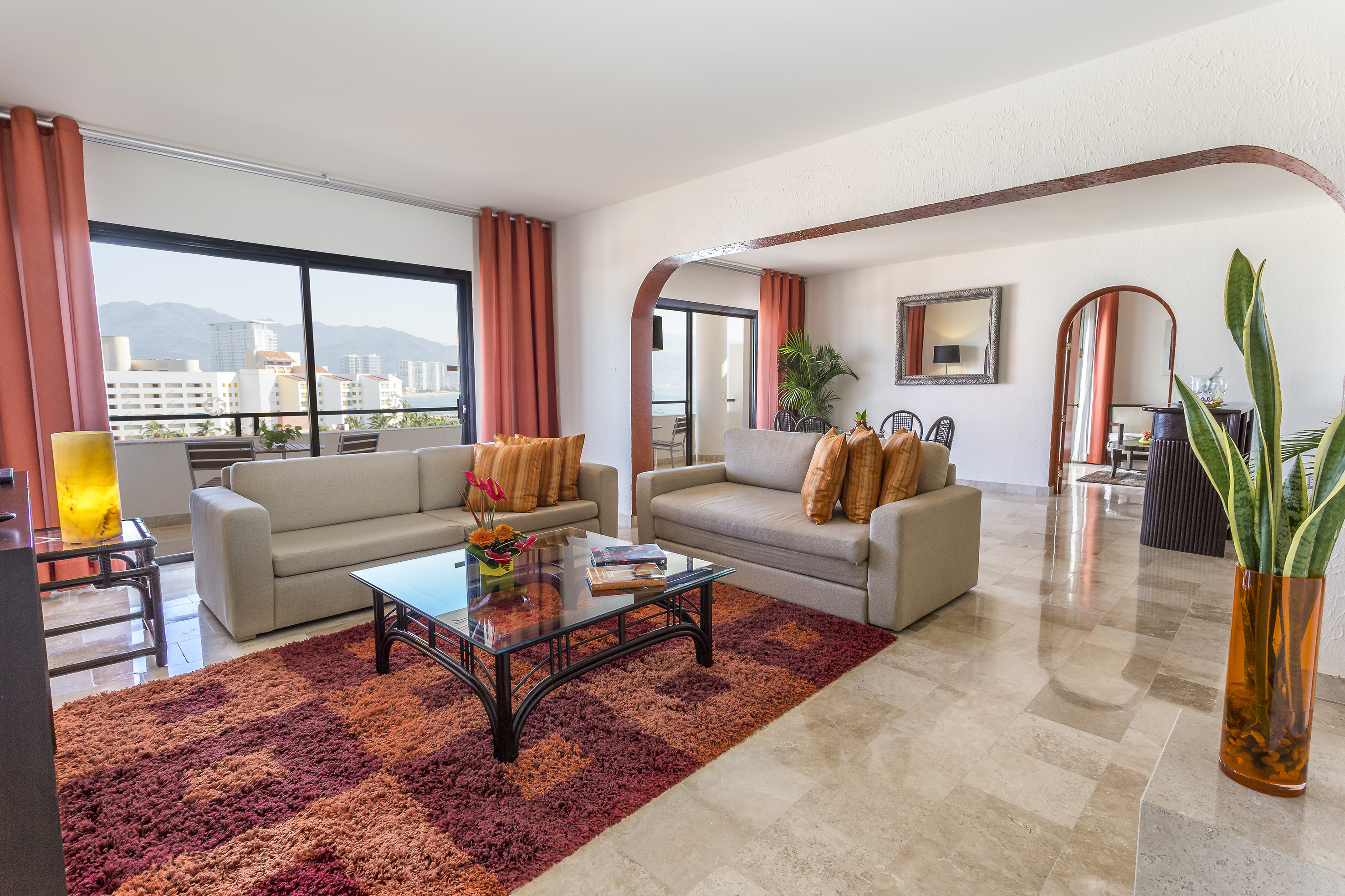 Balcony living room with ocean and mountain views, two sofas, and red rug.