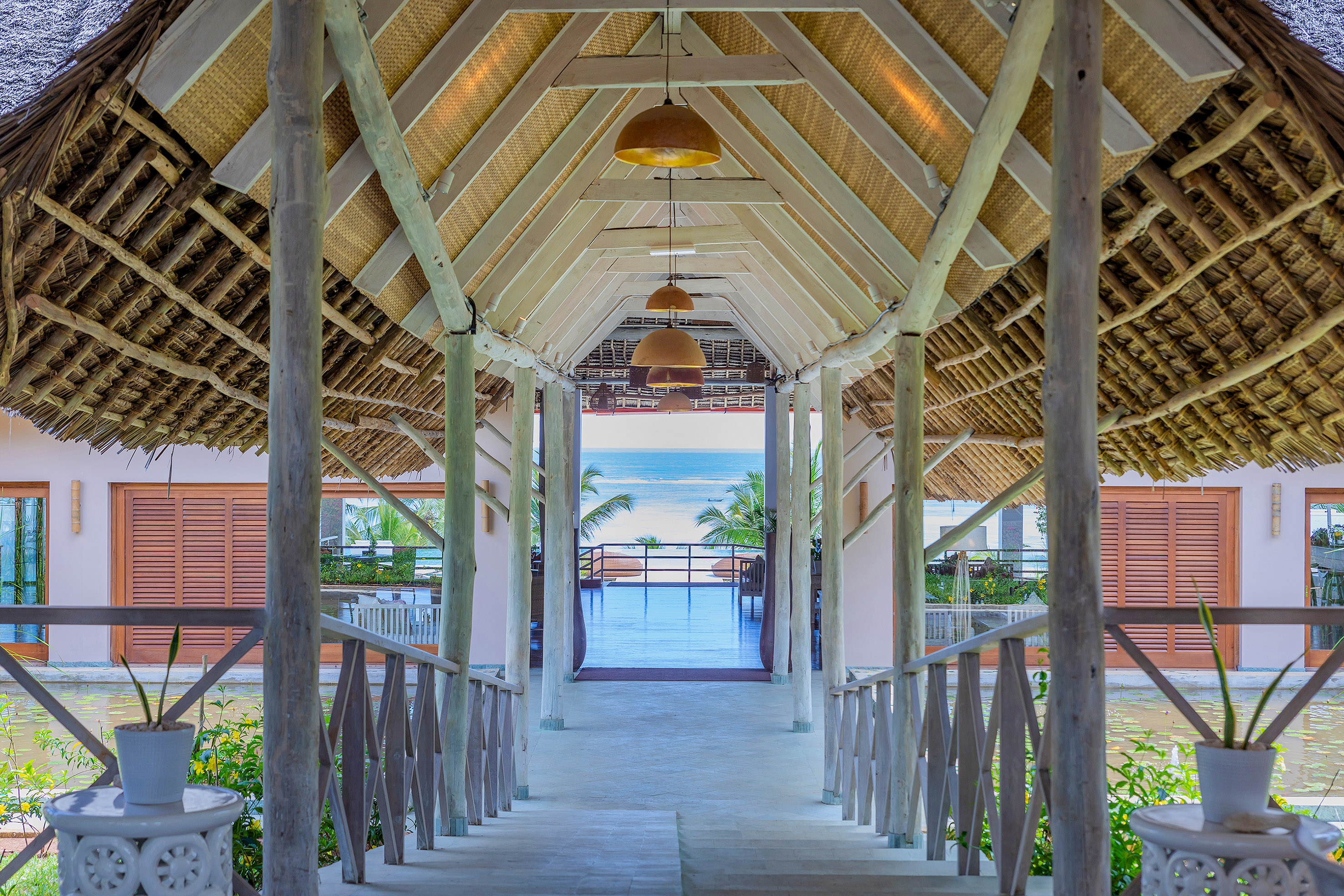 Thatched walkway leading to blue ocean view at a tropical resort.