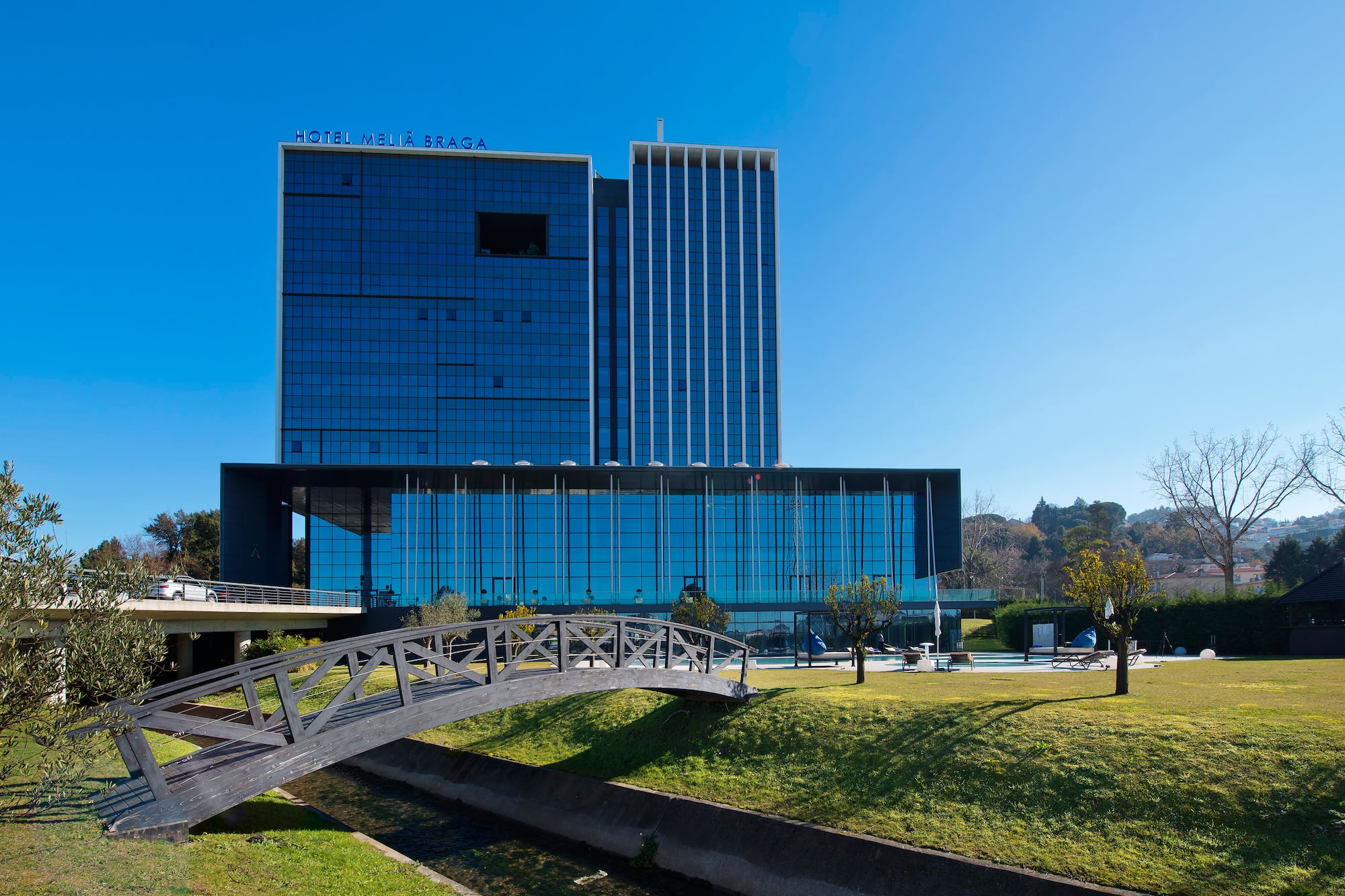 Hotel Meliã Braga: modern blue glass hotel with footbridge and pool area.