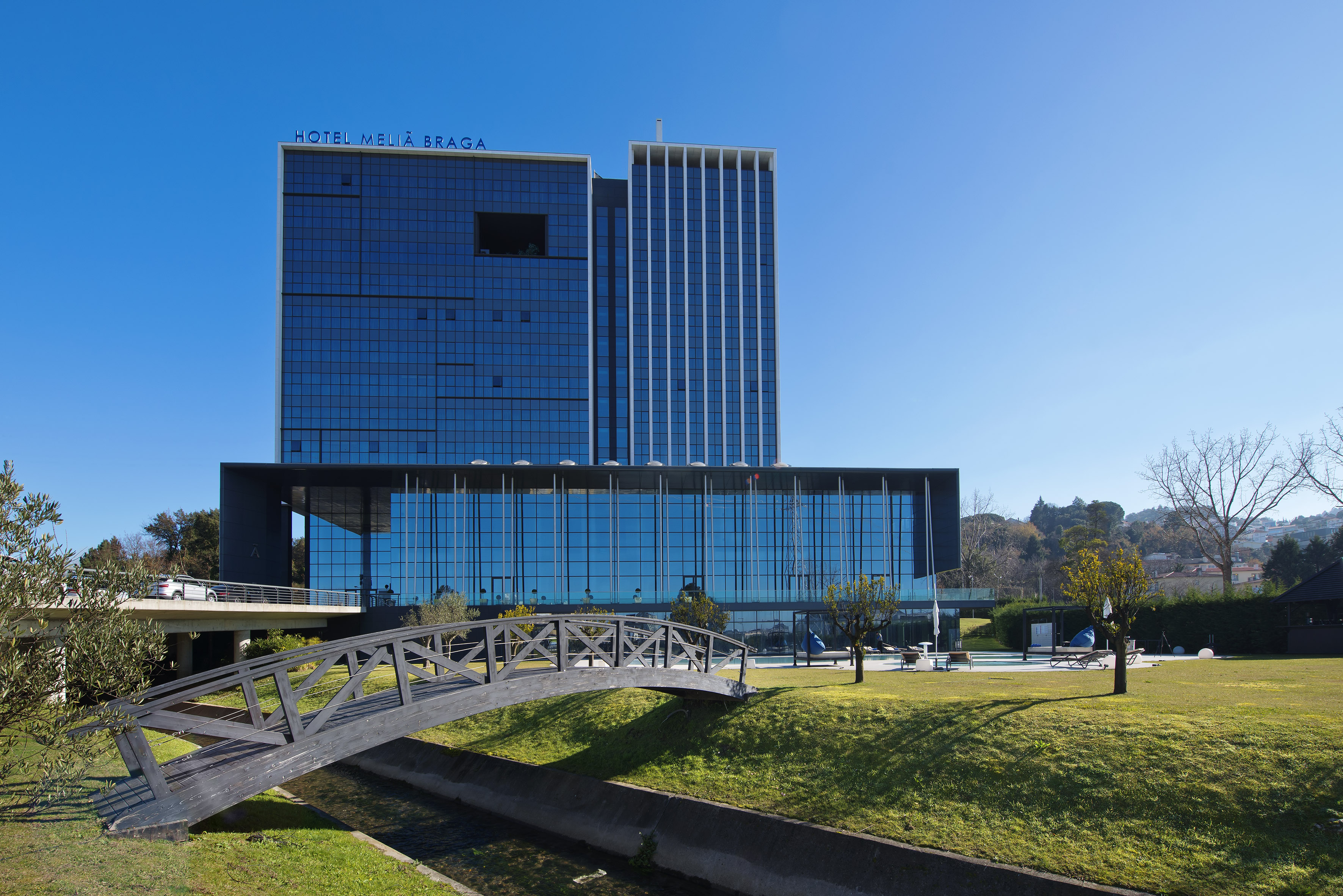 Hotel Meliã Braga: modern blue glass hotel with footbridge and pool area.
