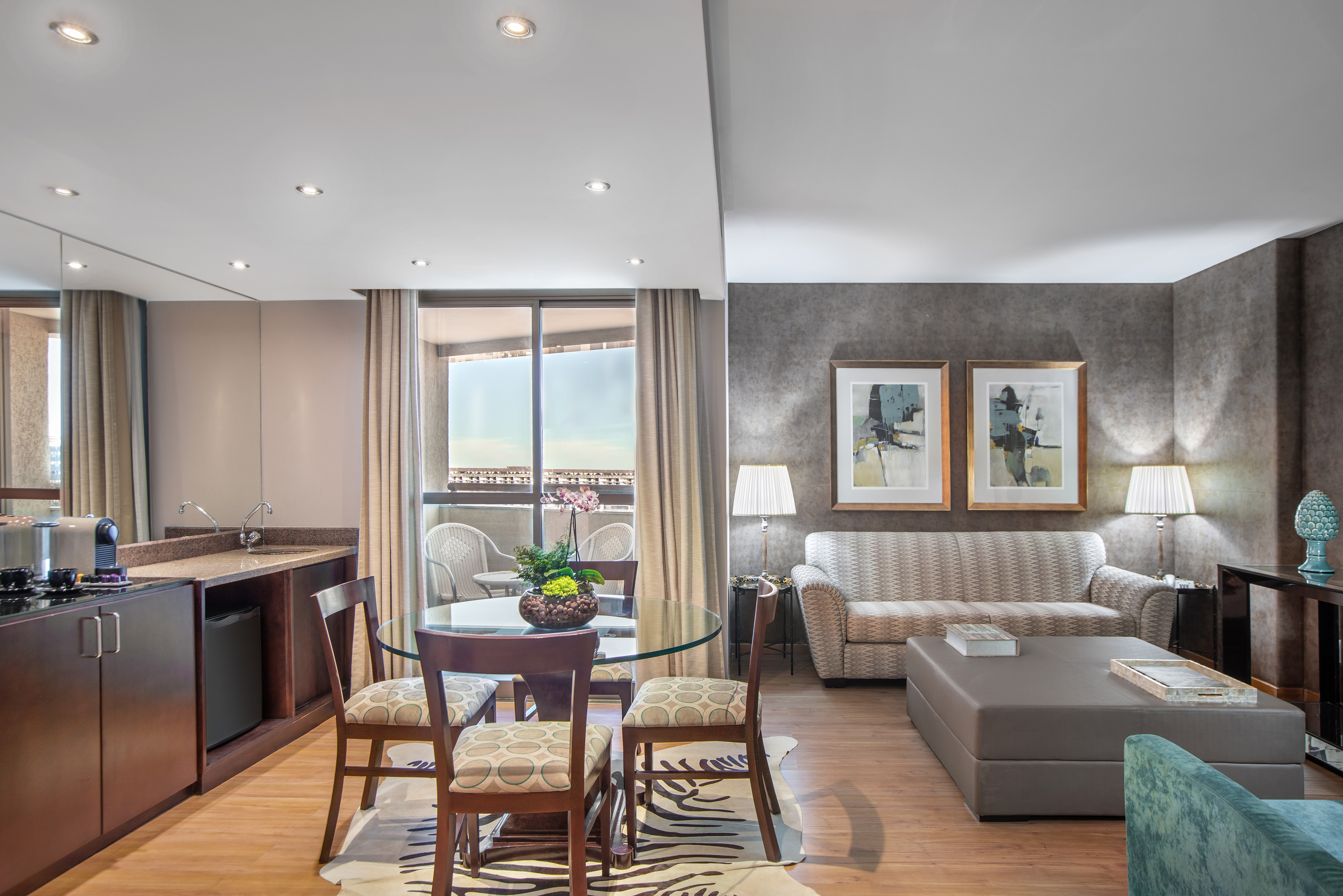 Modern hotel suite with living, dining, kitchenette, and balcony.