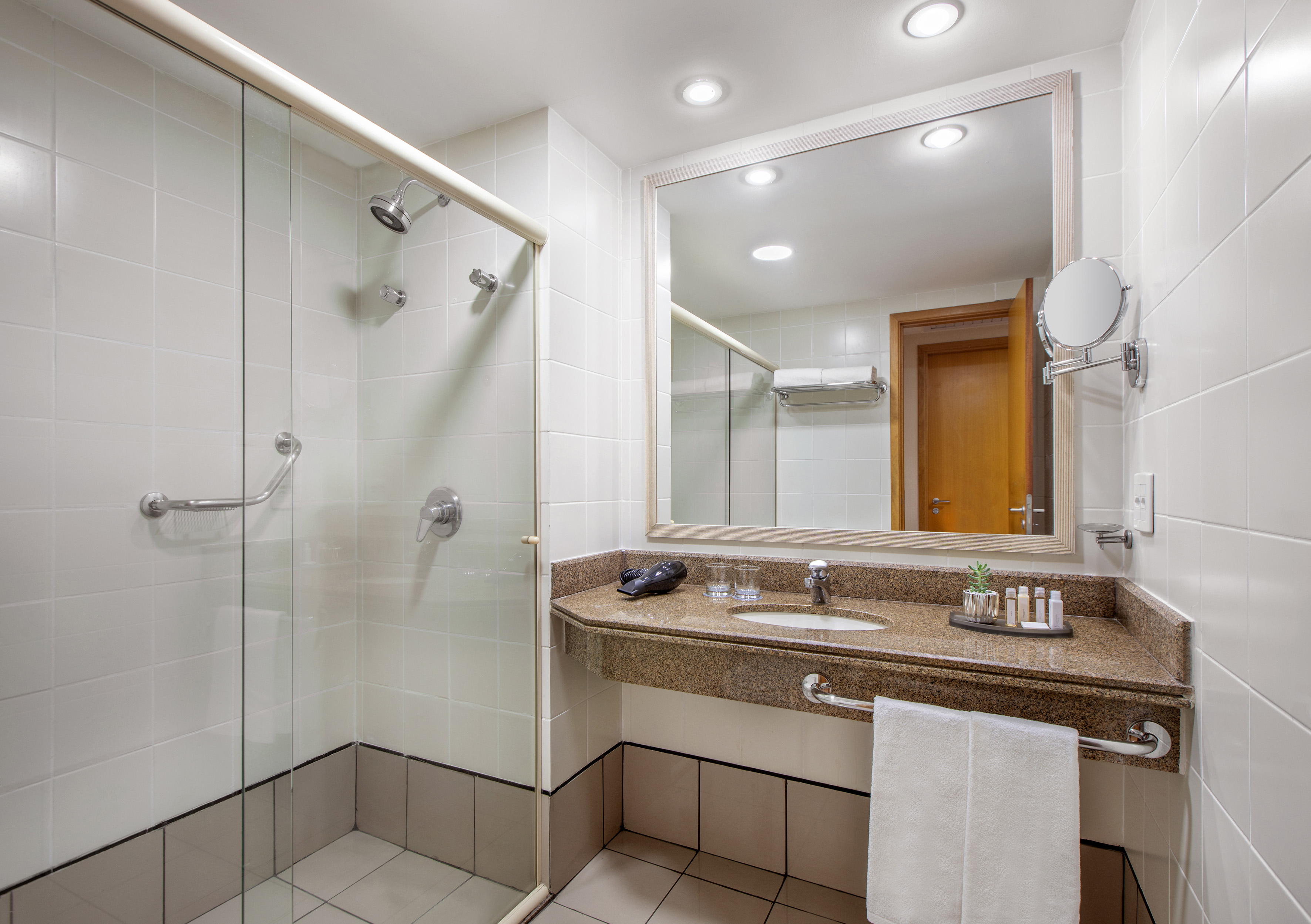 Modern hotel bathroom with accessible shower, granite vanity, and large mirror.