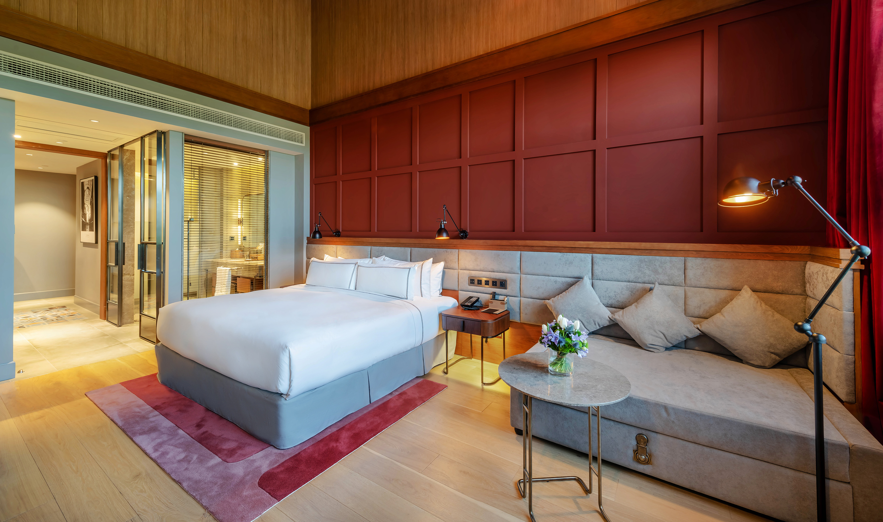Modern hotel bedroom with red accent wall, king bed, and built-in sofa.