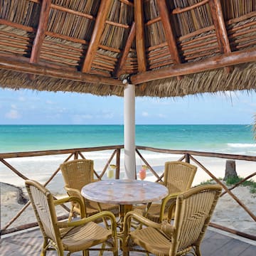 a table and chairs under a thatched roof on a beach