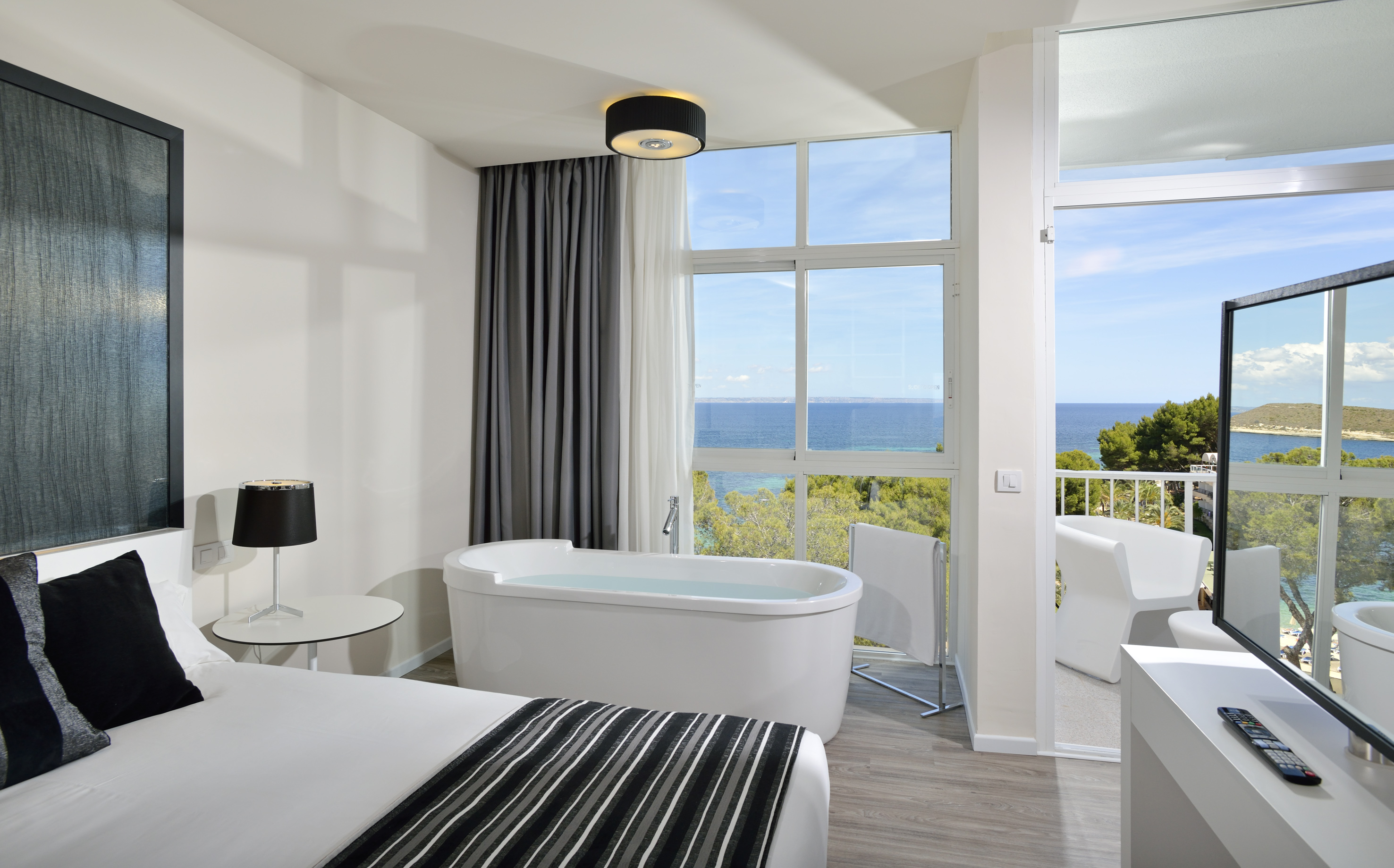 Modern hotel room with sea view, freestanding bathtub, and balcony.