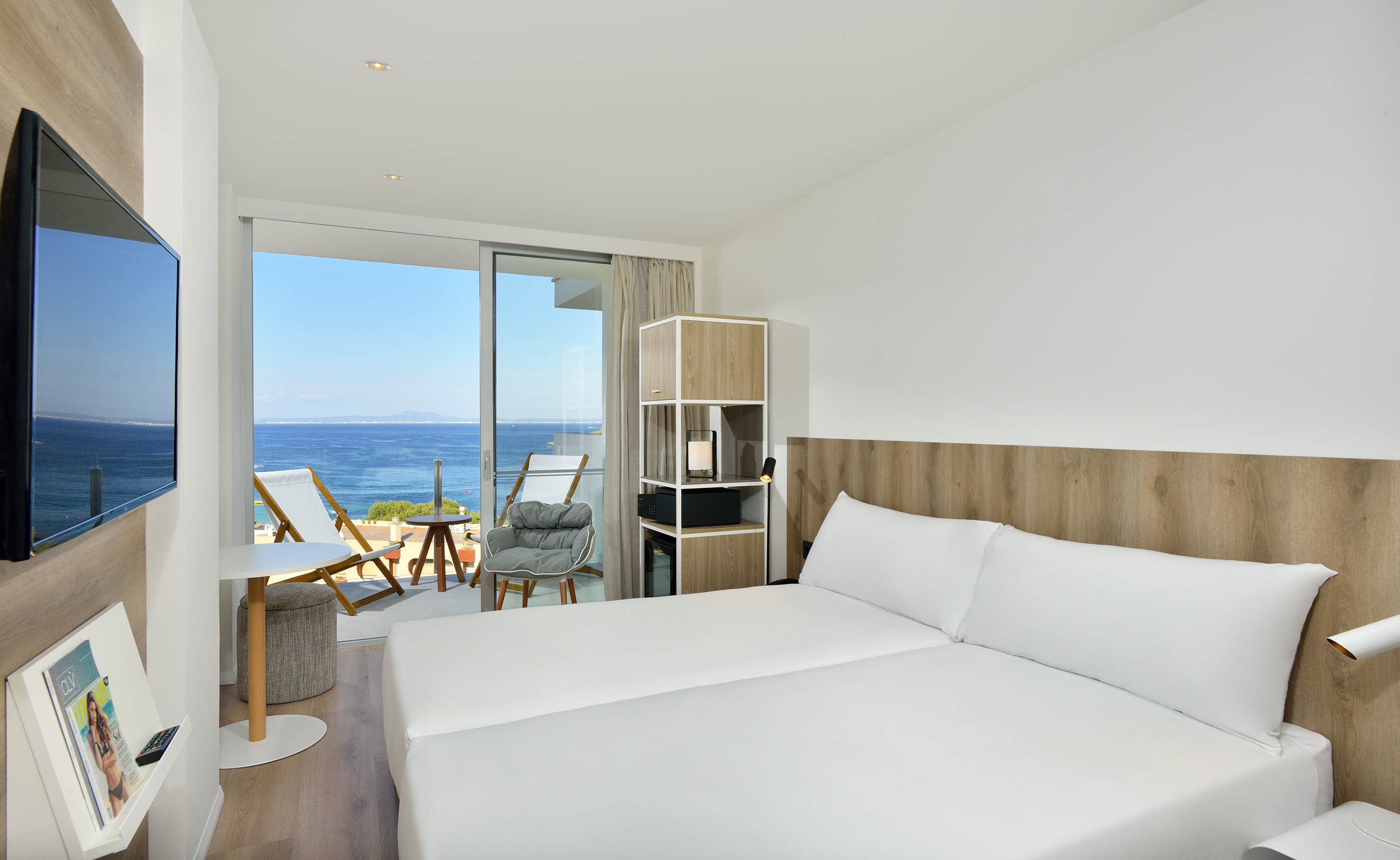 Bright hotel room with ocean view balcony and modern white bed.