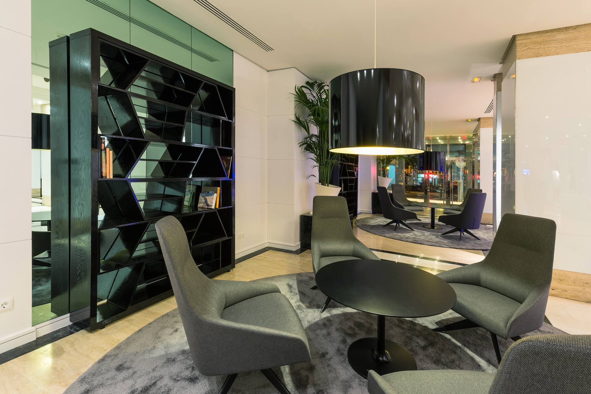 Modern hotel lounge with gray chairs, black table, geometric bookshelf.