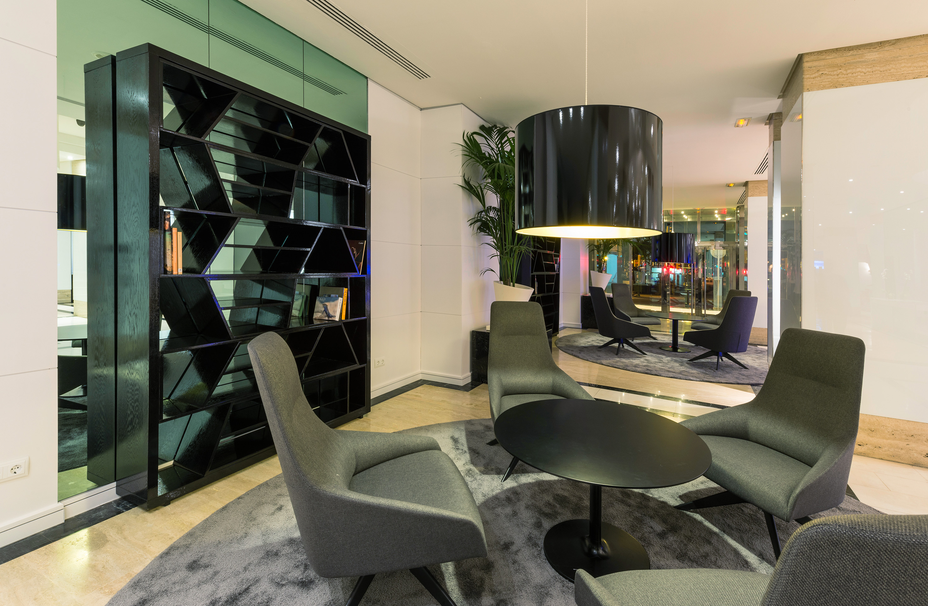 Modern hotel lounge with gray chairs, black table, geometric bookshelf.