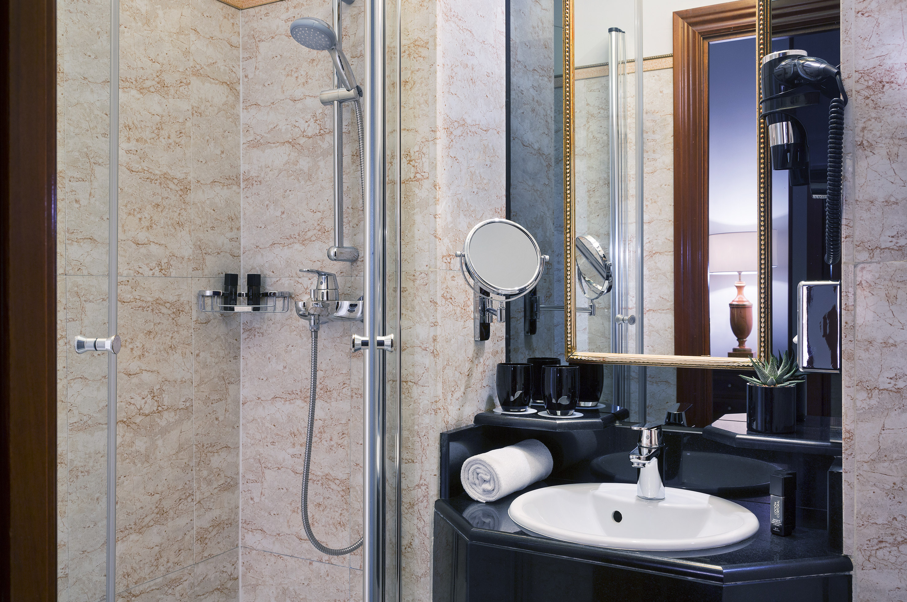 Modern hotel bathroom with marble walls, shower, vanity, sink, and mirror.