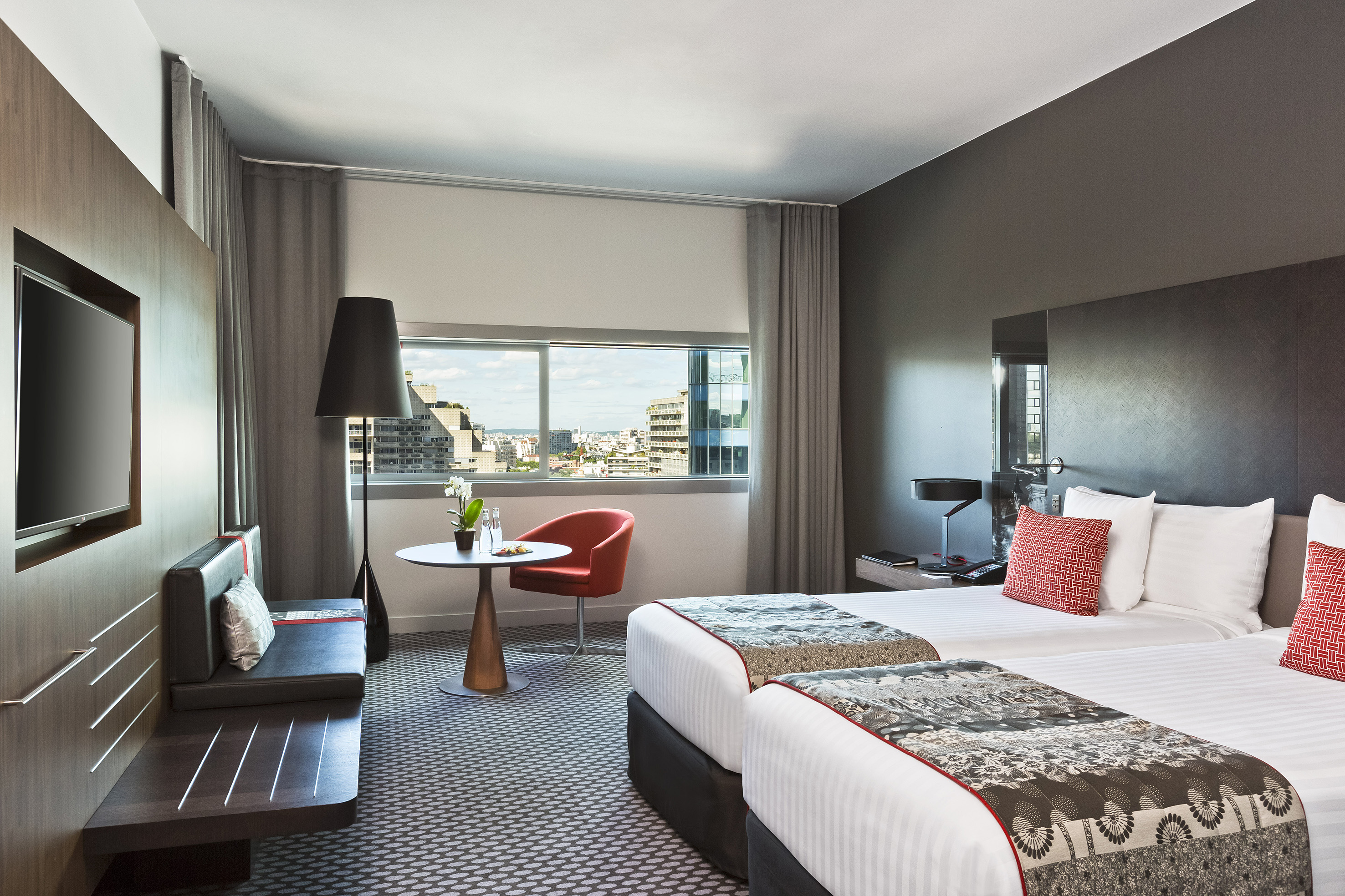 Modern hotel room with twin beds, city view window, and a lounge area.