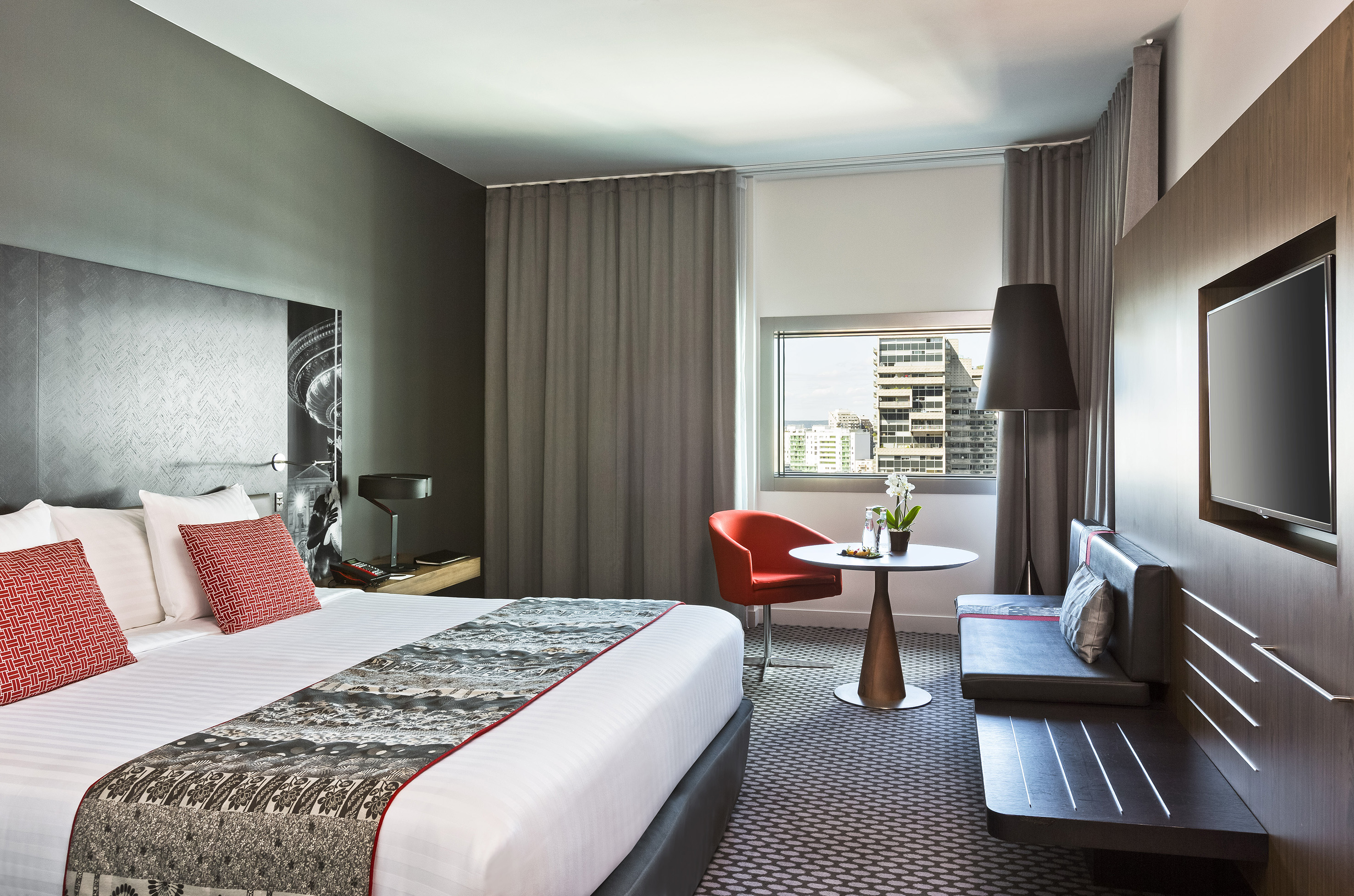Contemporary hotel bedroom with king bed, city skyline view, and TV.