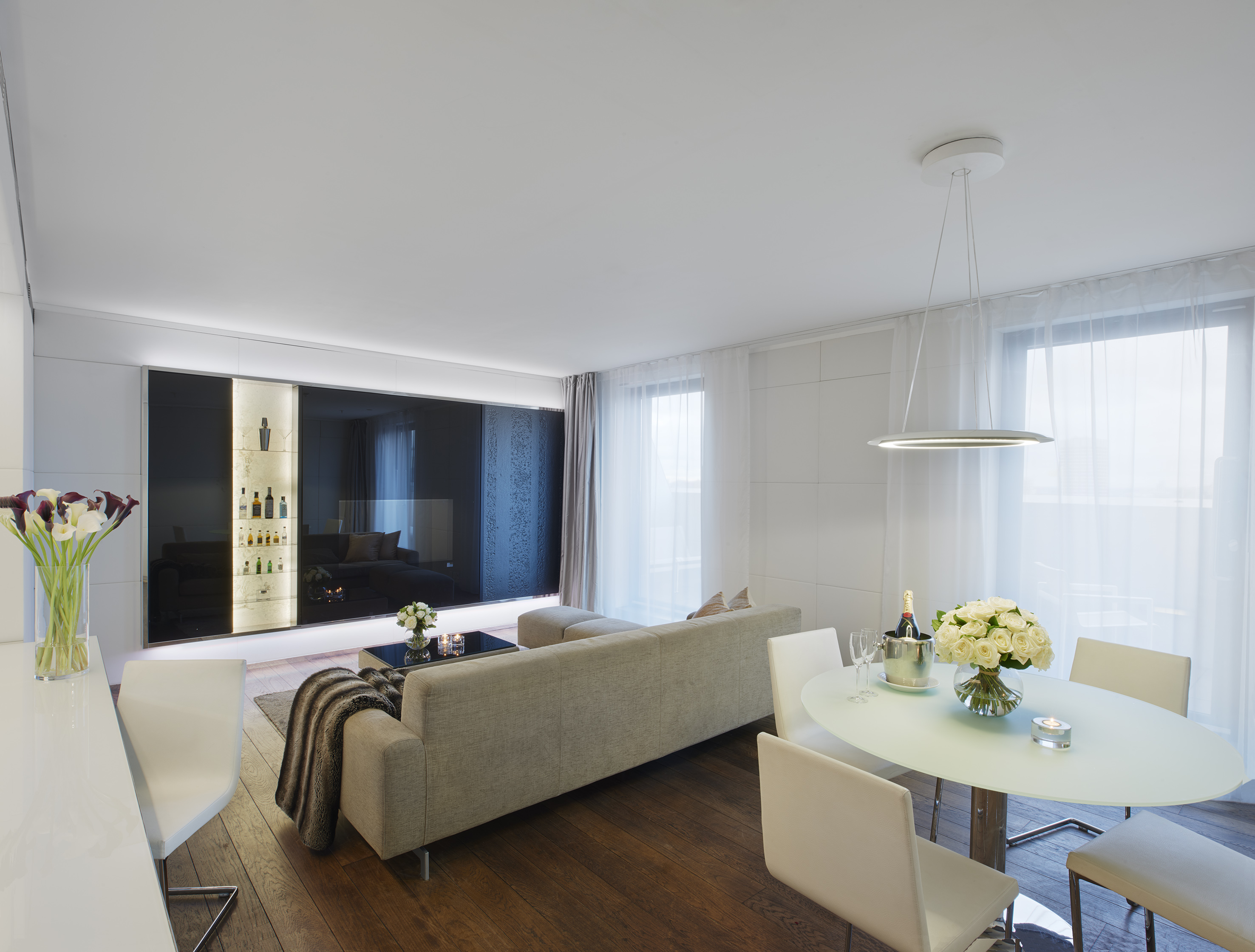 Modern open-plan living and dining room with beige sofa, wood floor, backlit bar.