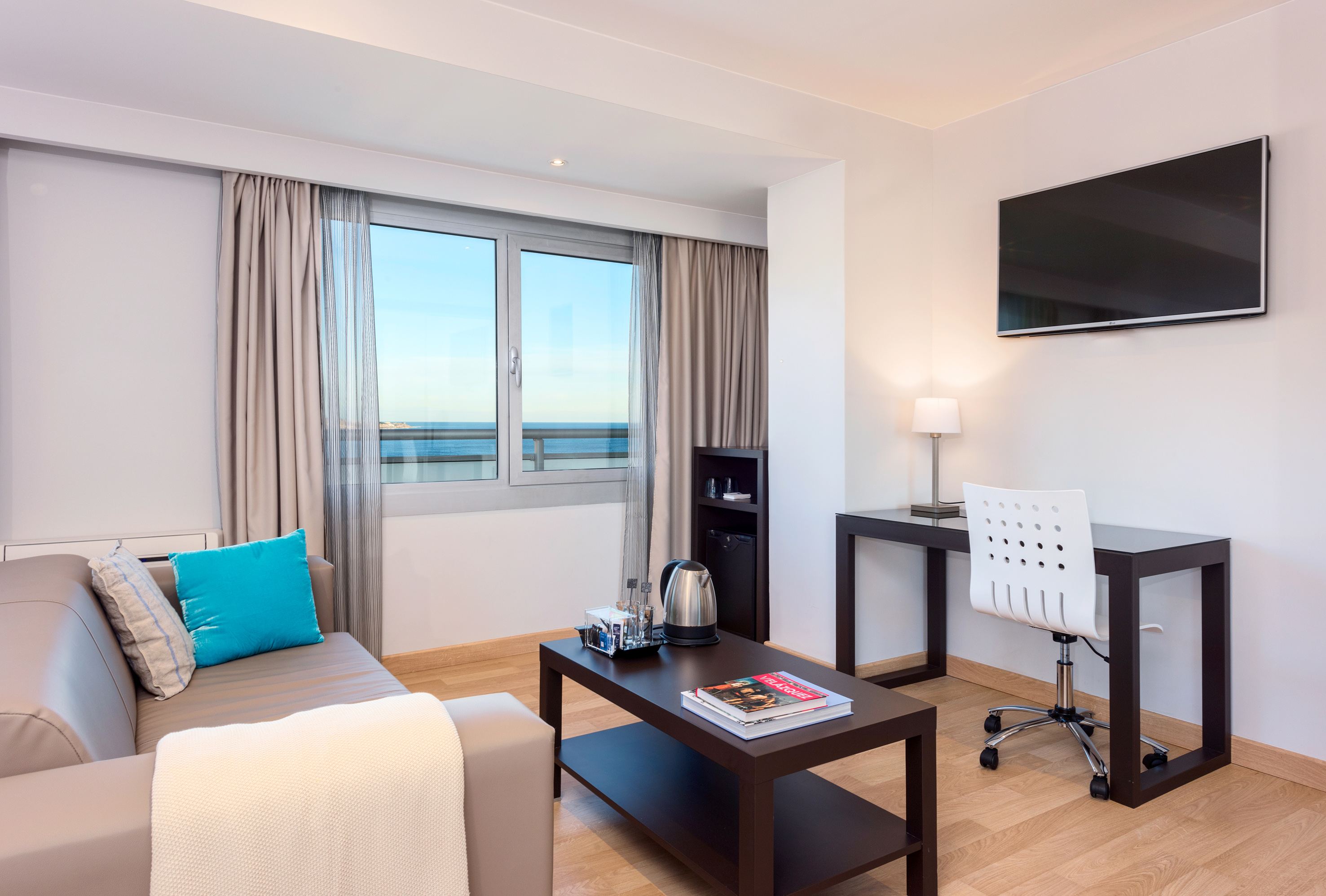 Modern hotel suite with ocean view, sofa, coffee table, and workspace.