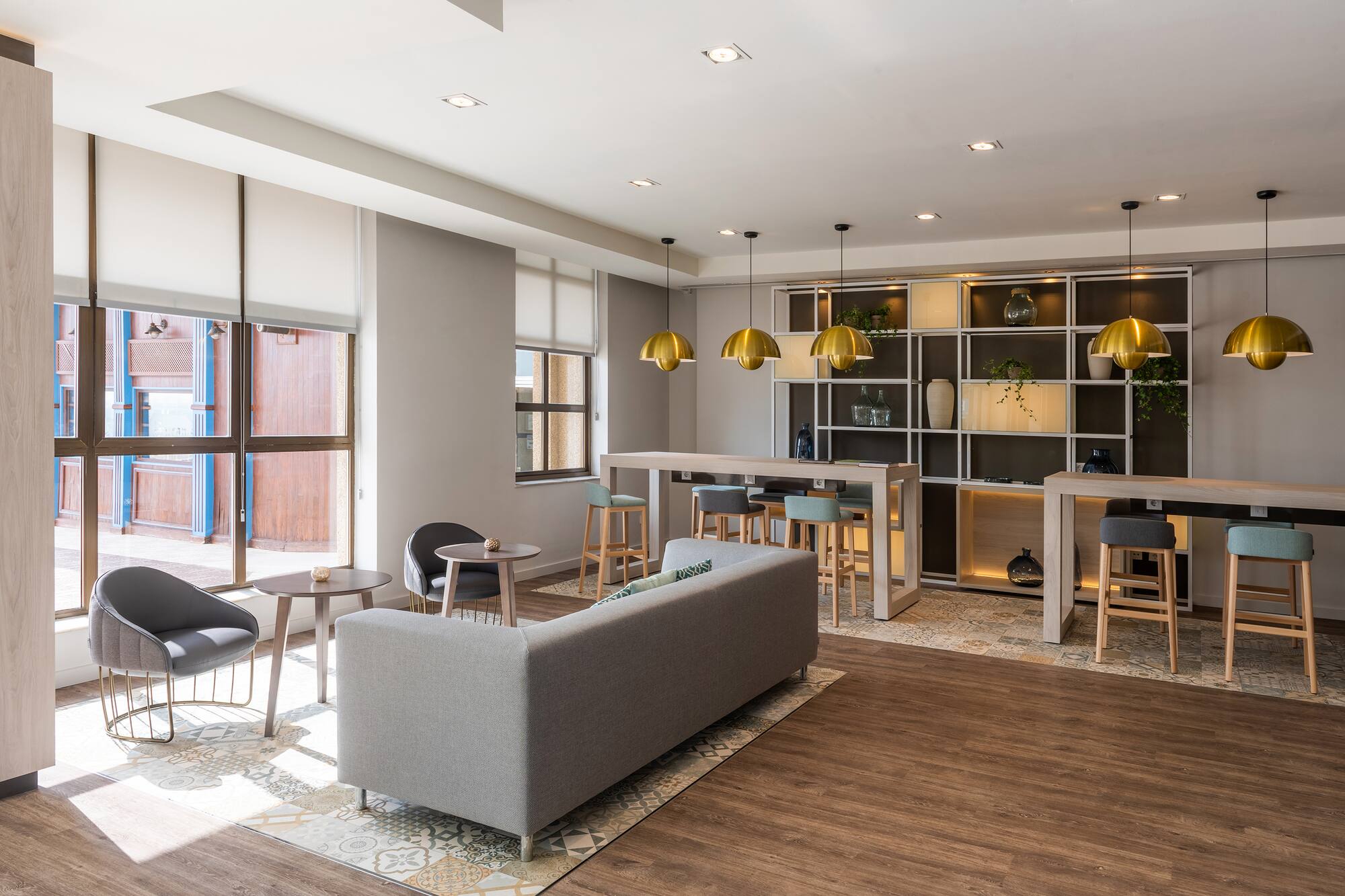 Modern lounge interior with grey sofa, bar tables, gold pendant lights, wood floor.