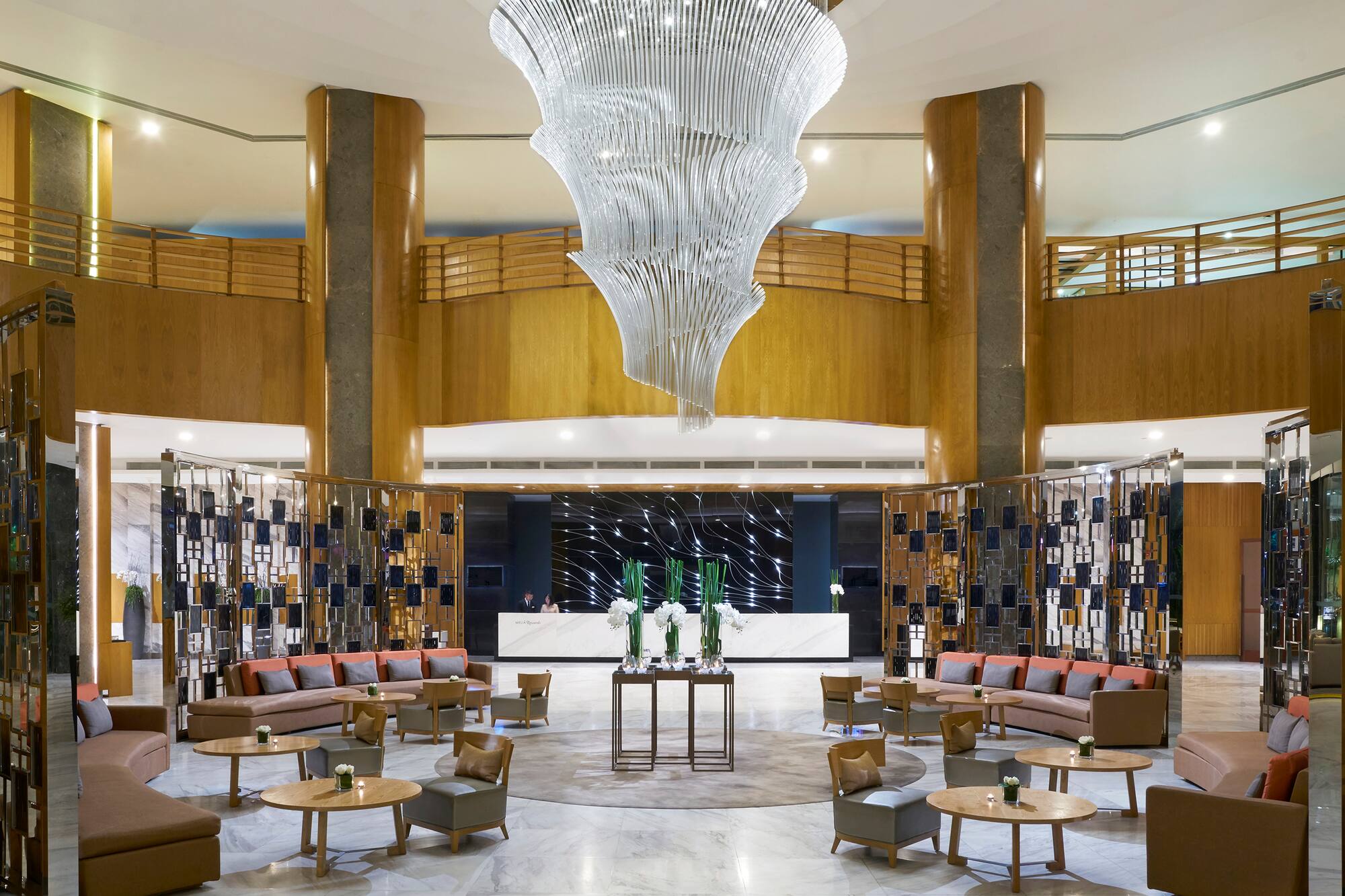 Grand hotel lobby with swirling chandelier, reception desk, and modern lounge seating.