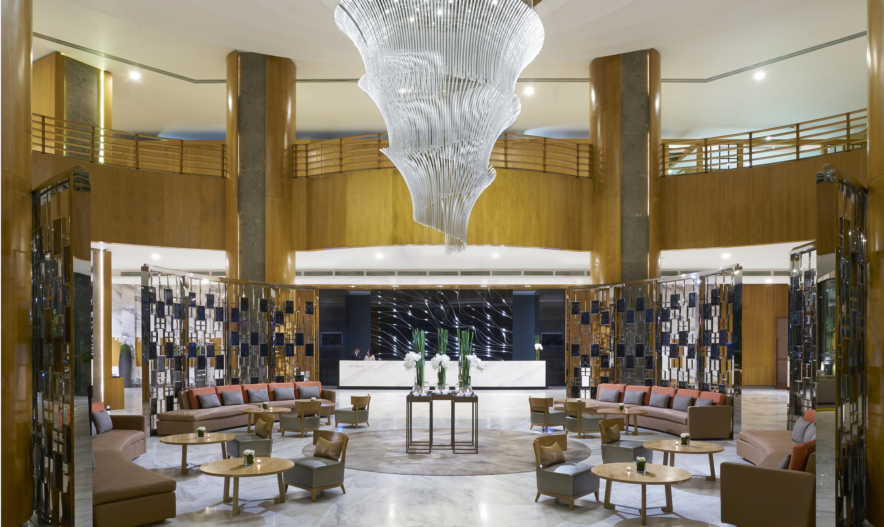 Grand hotel lobby with swirling chandelier, reception desk, and modern lounge seating.