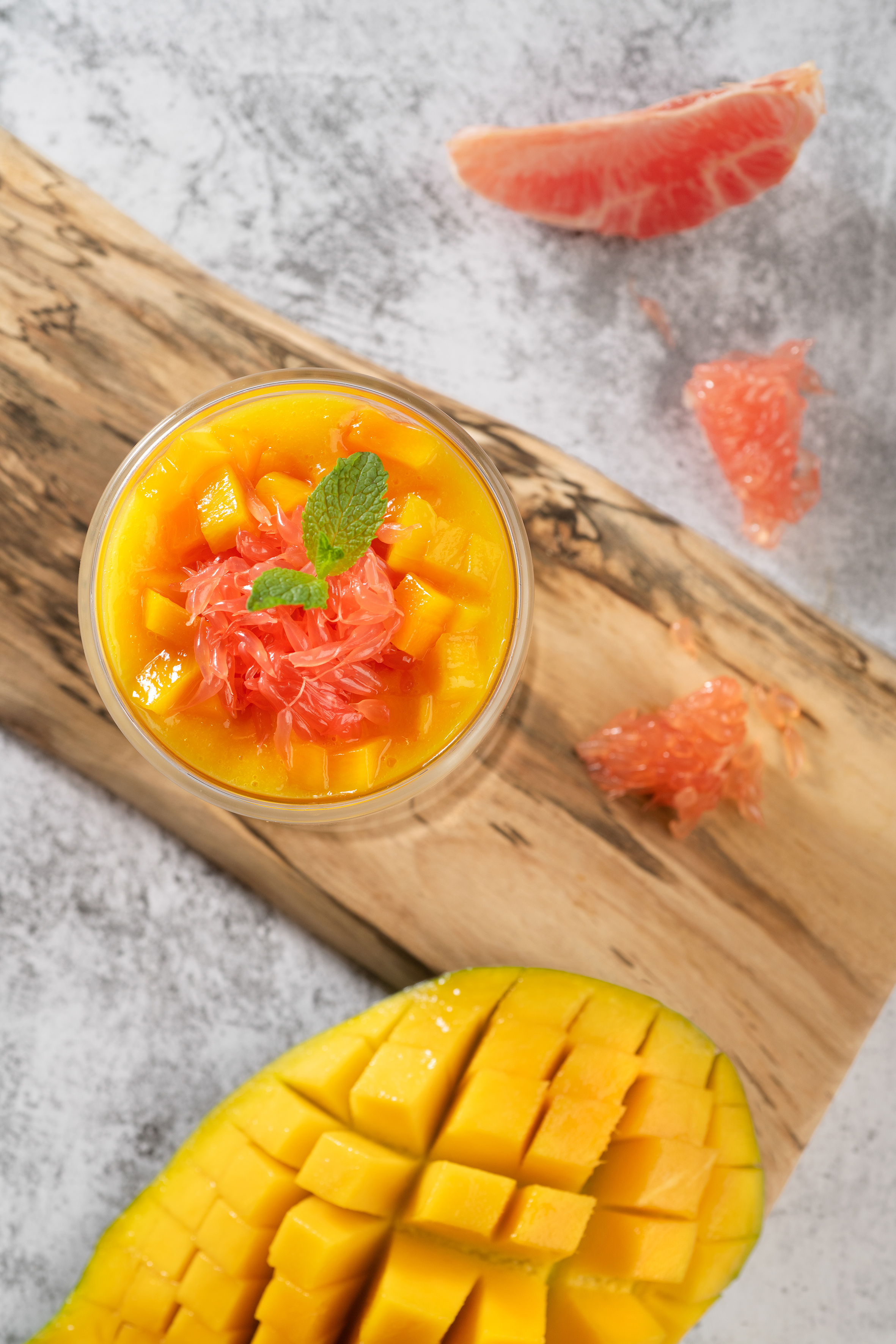 Fresh mango and grapefruit dessert with mint on a wooden board.
