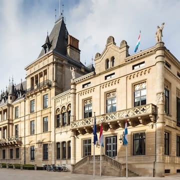 a large stone building with flags with Grand Ducal Palace, Luxembourg in the background