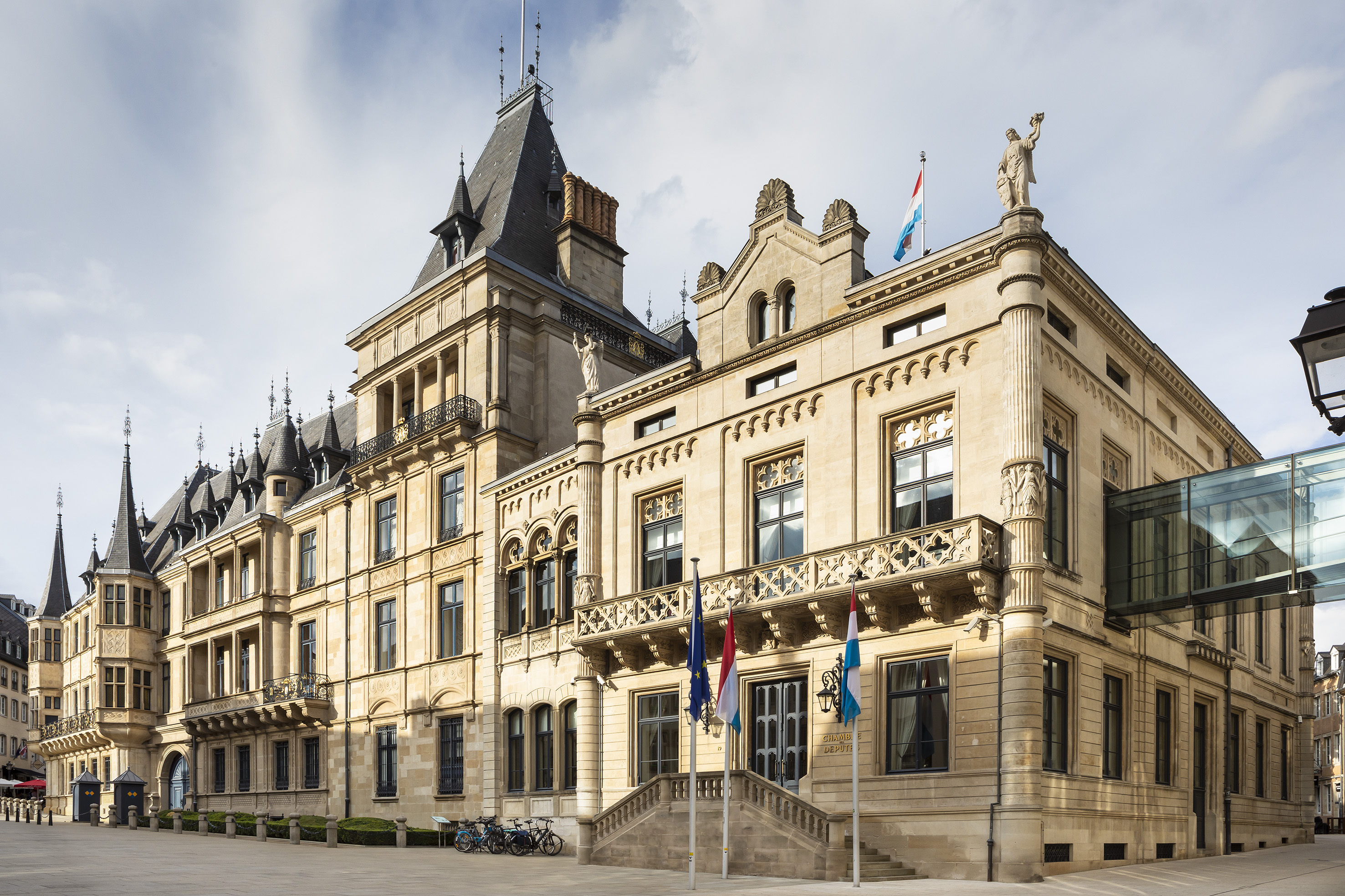 Ornate stone Chambre des Députés, Luxembourg Parliament, flags, glass bridge.
