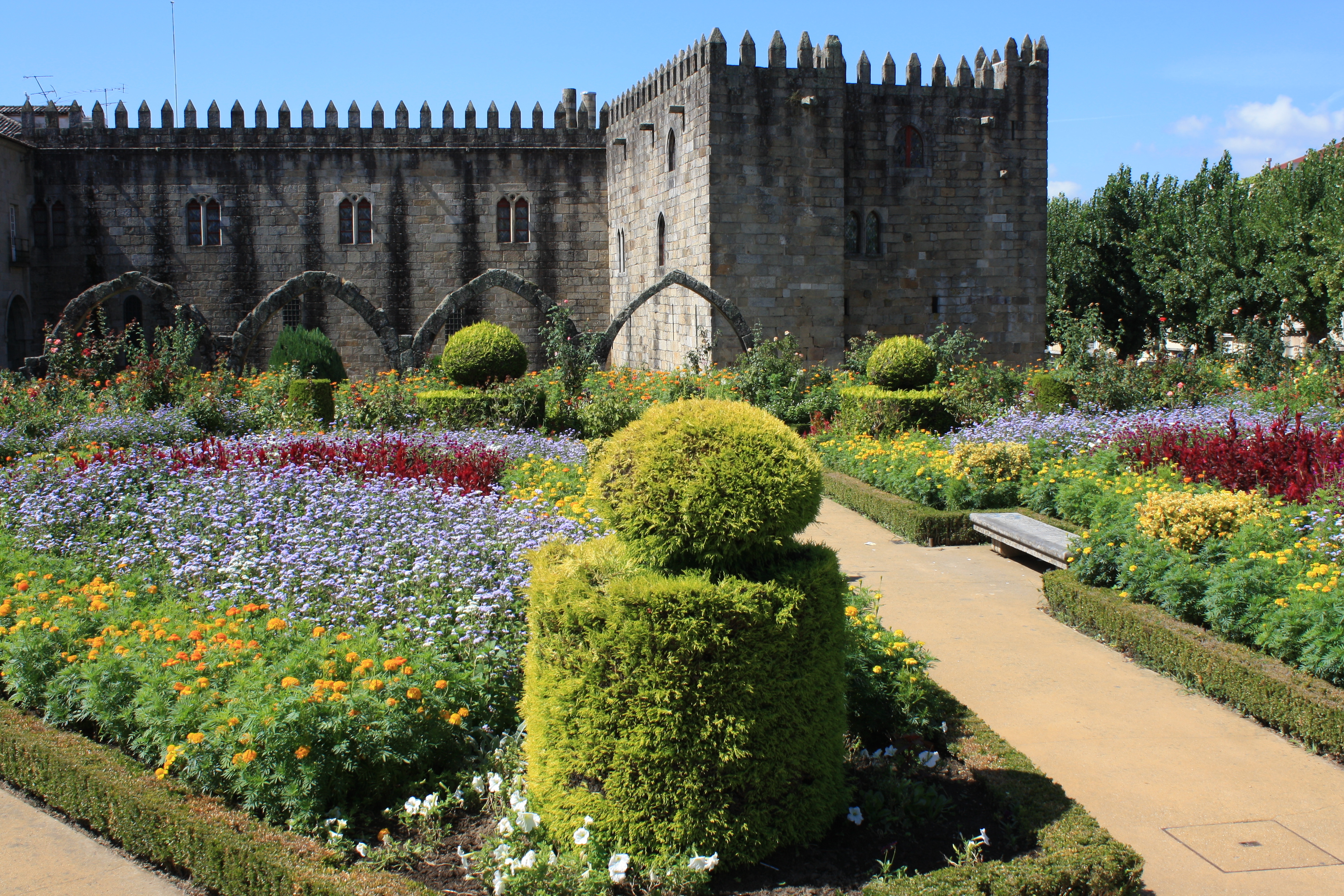 Vibrant flower gardens and topiary in front of a historic stone castle.