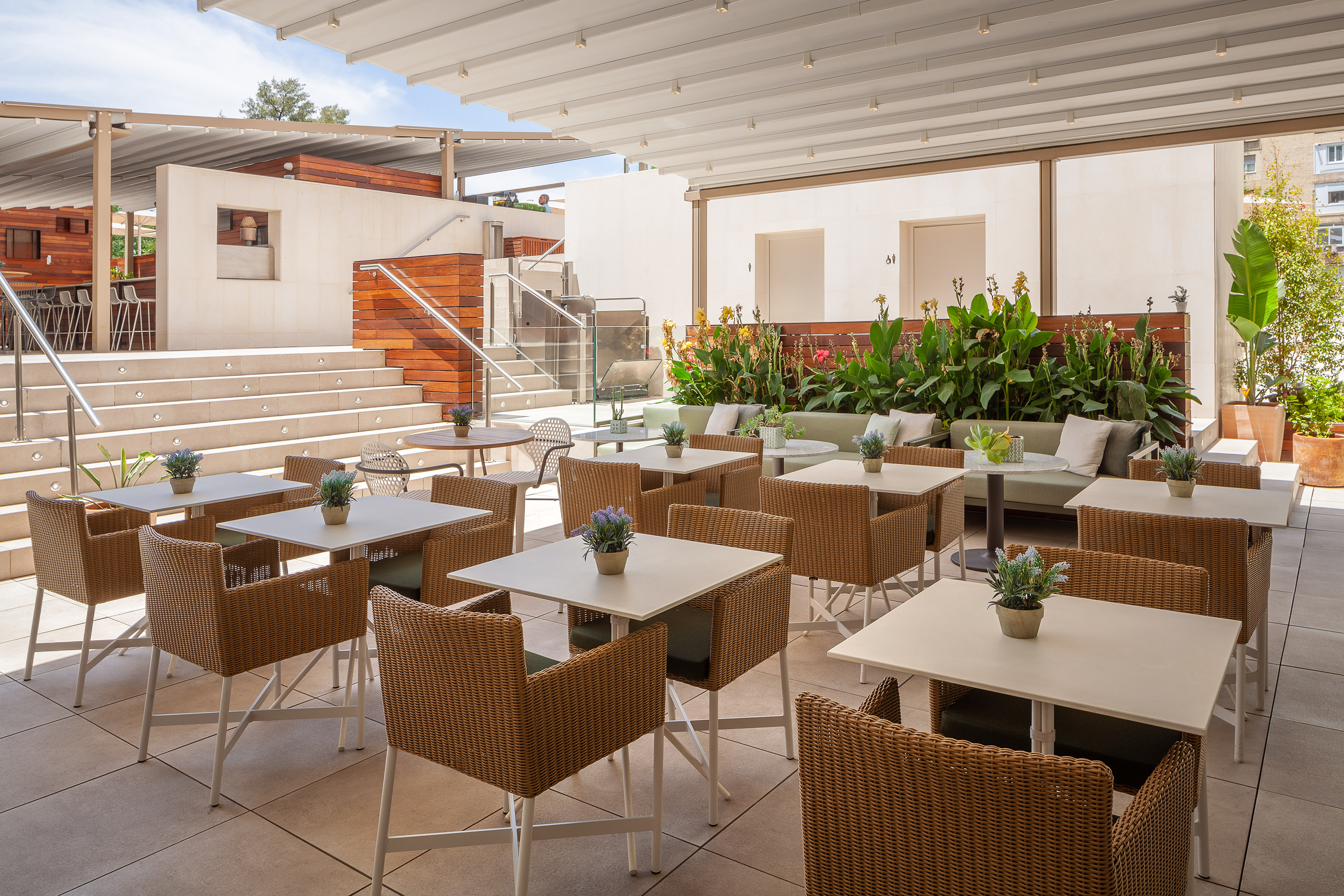 Modern al fresco dining patio with wicker chairs, square tables, and plants.
