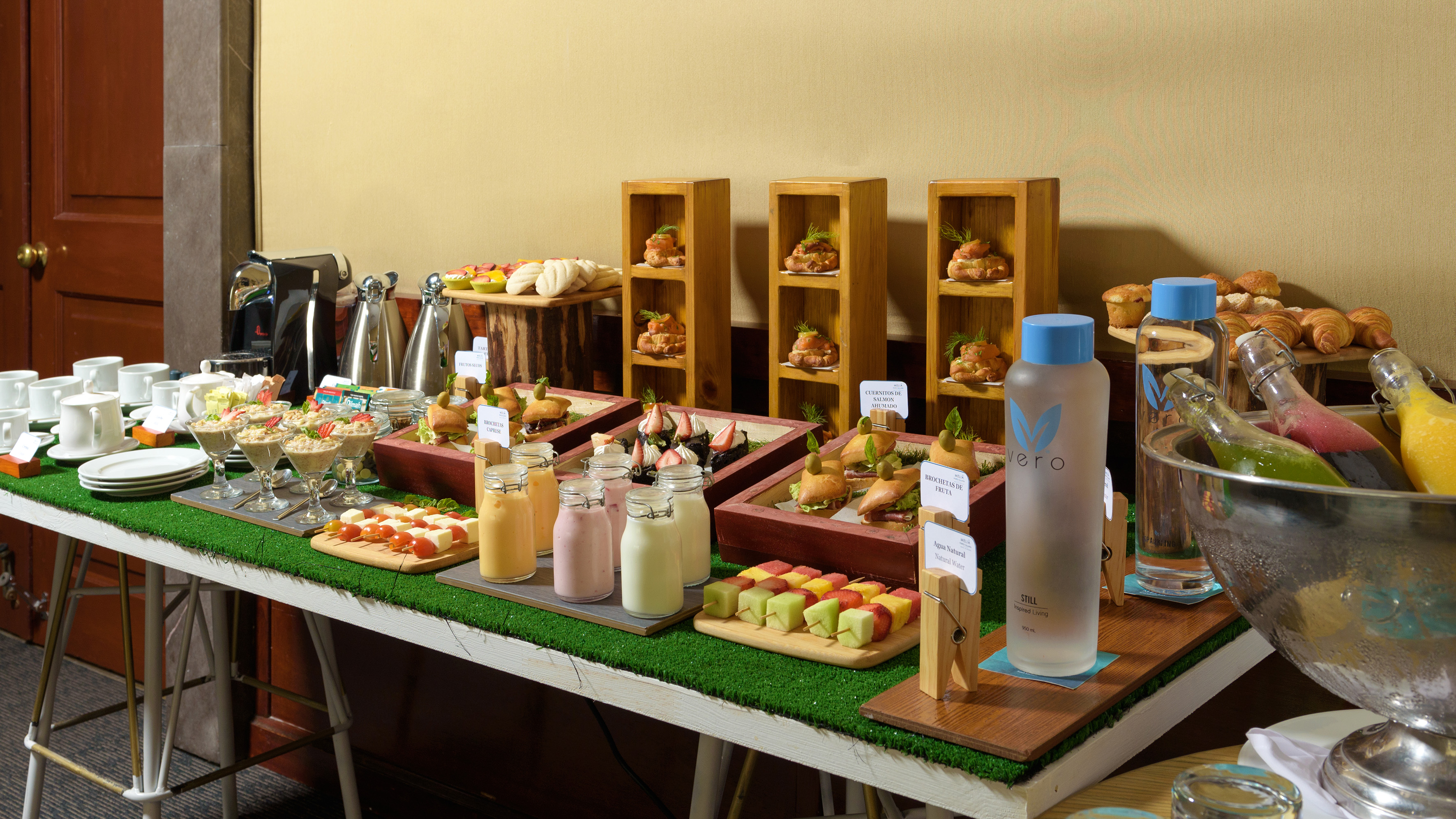 Breakfast buffet featuring mini sandwiches, fruit, pastries, coffee, and Vero water bottles.