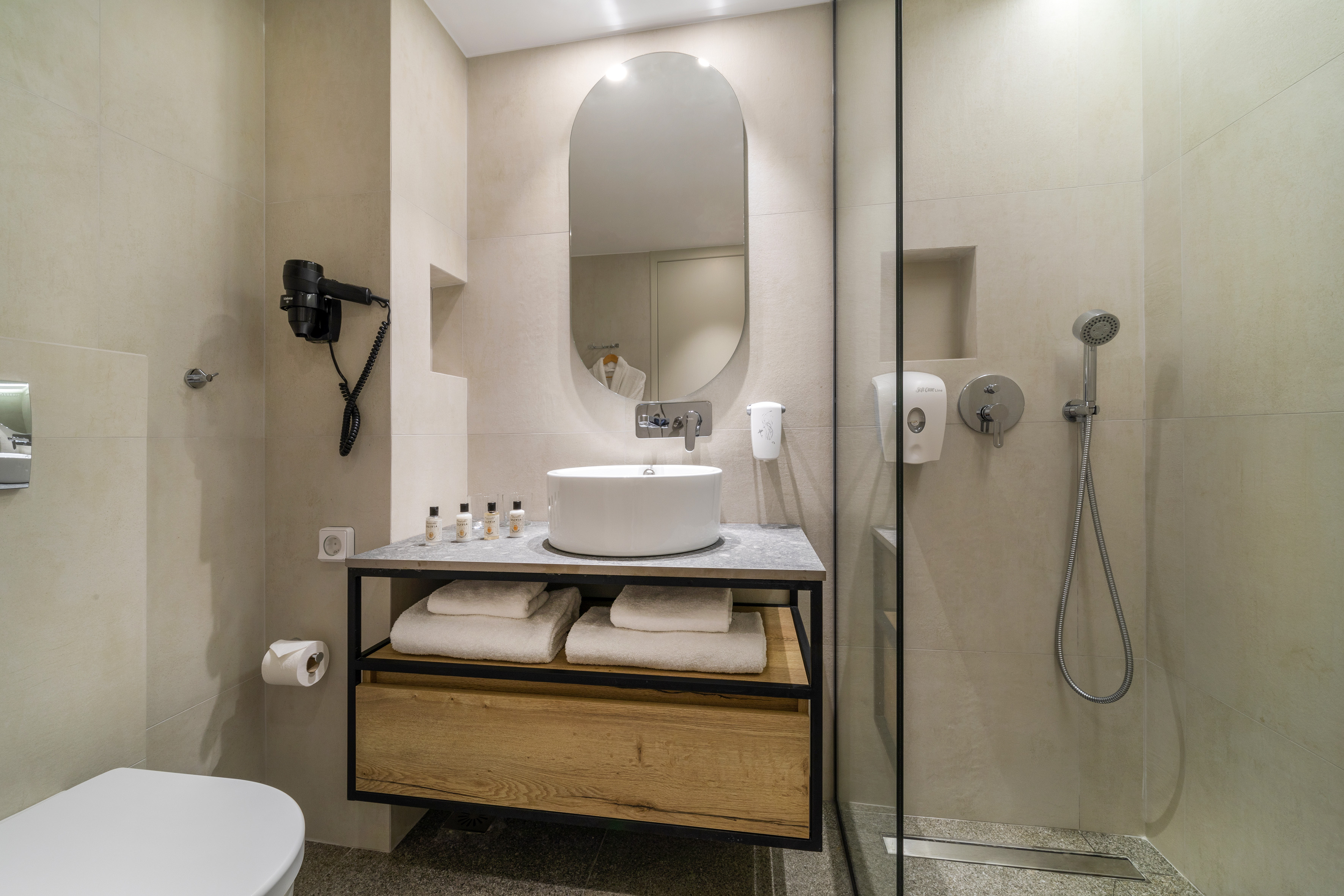 Modern beige bathroom: vanity with round sink, mirror, glass shower, toilet.