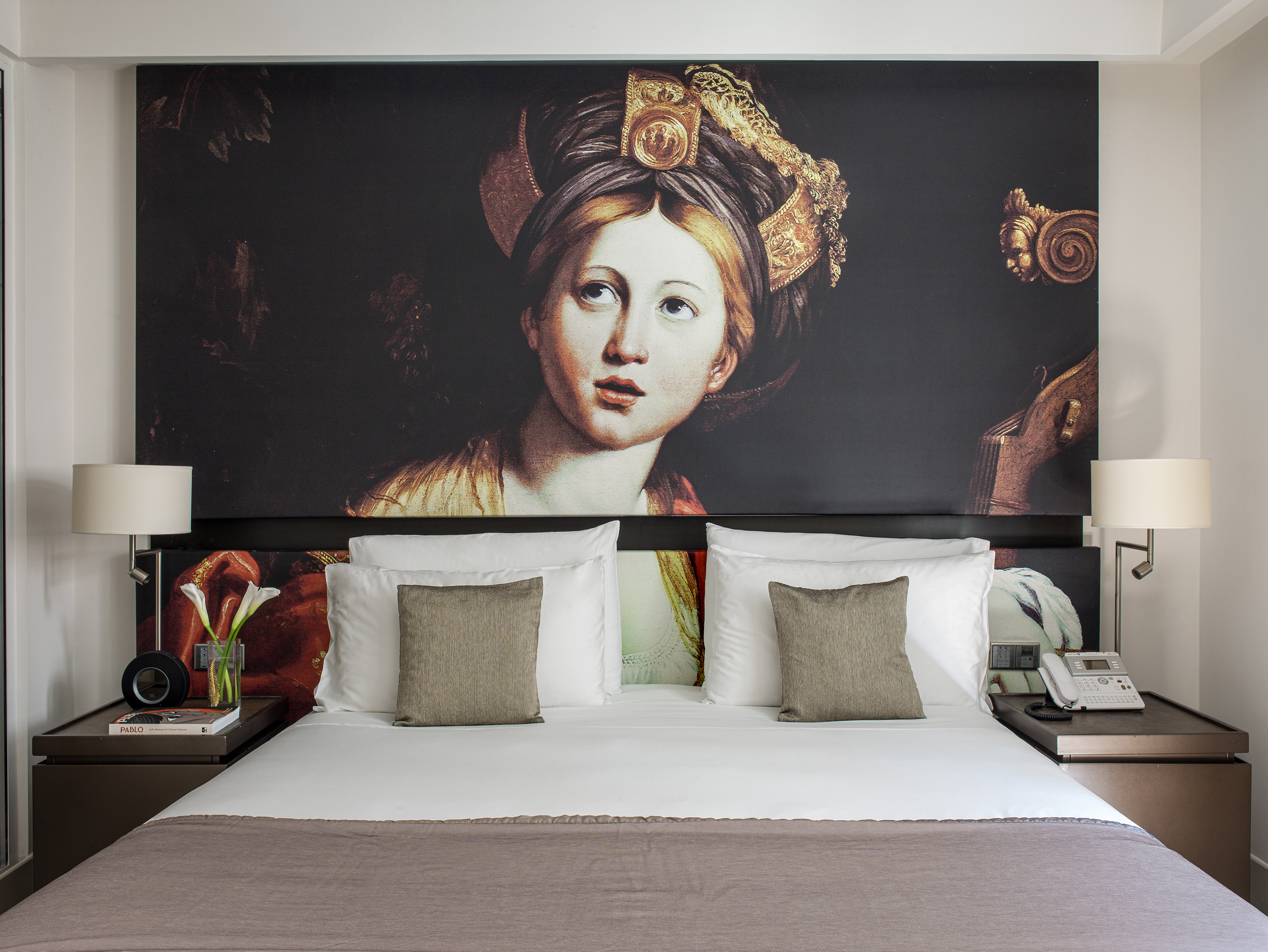 Hotel bedroom with large classical portrait mural headboard and white bed.