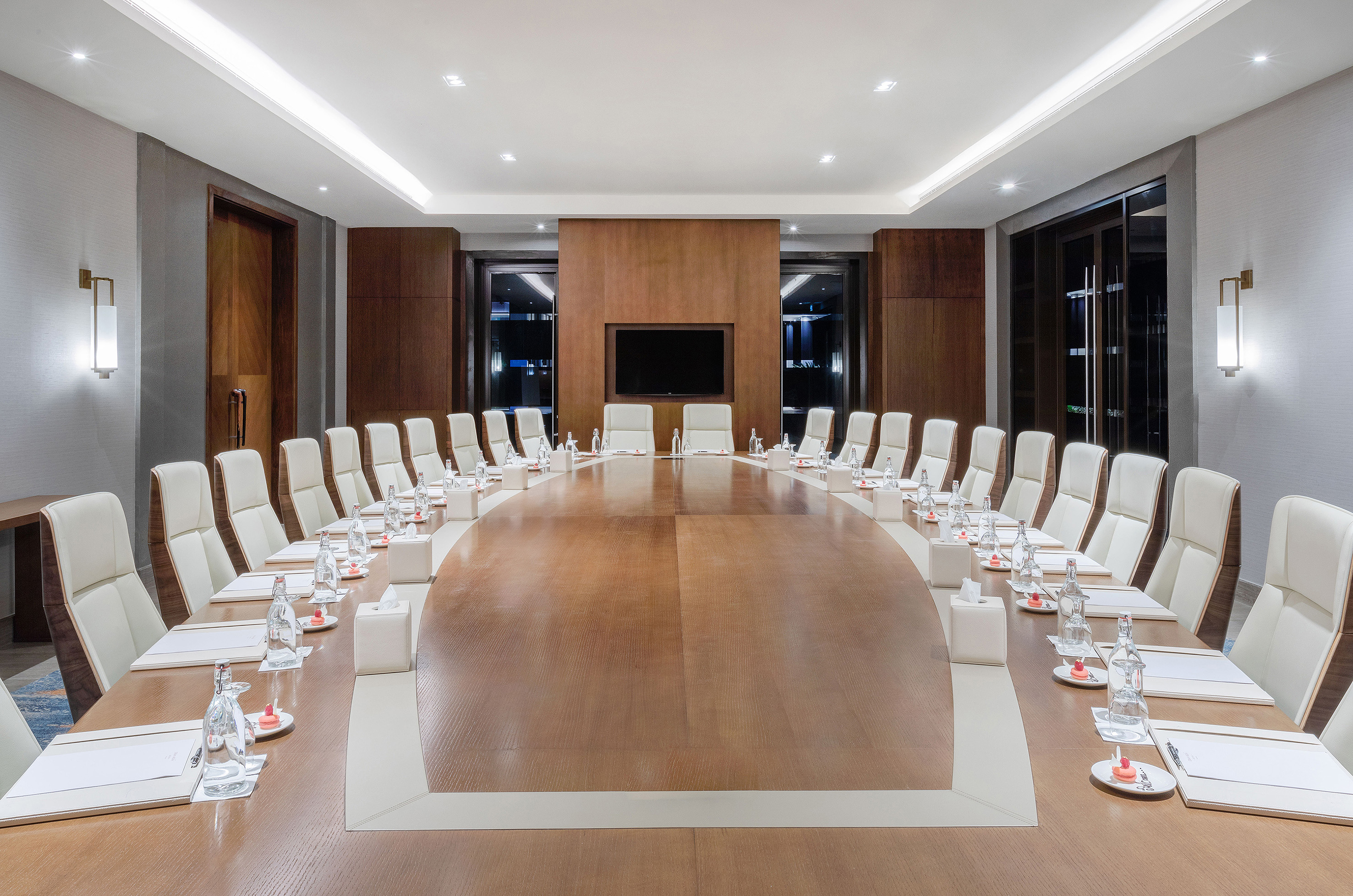 Modern executive boardroom with large oval table, white chairs, and TV.