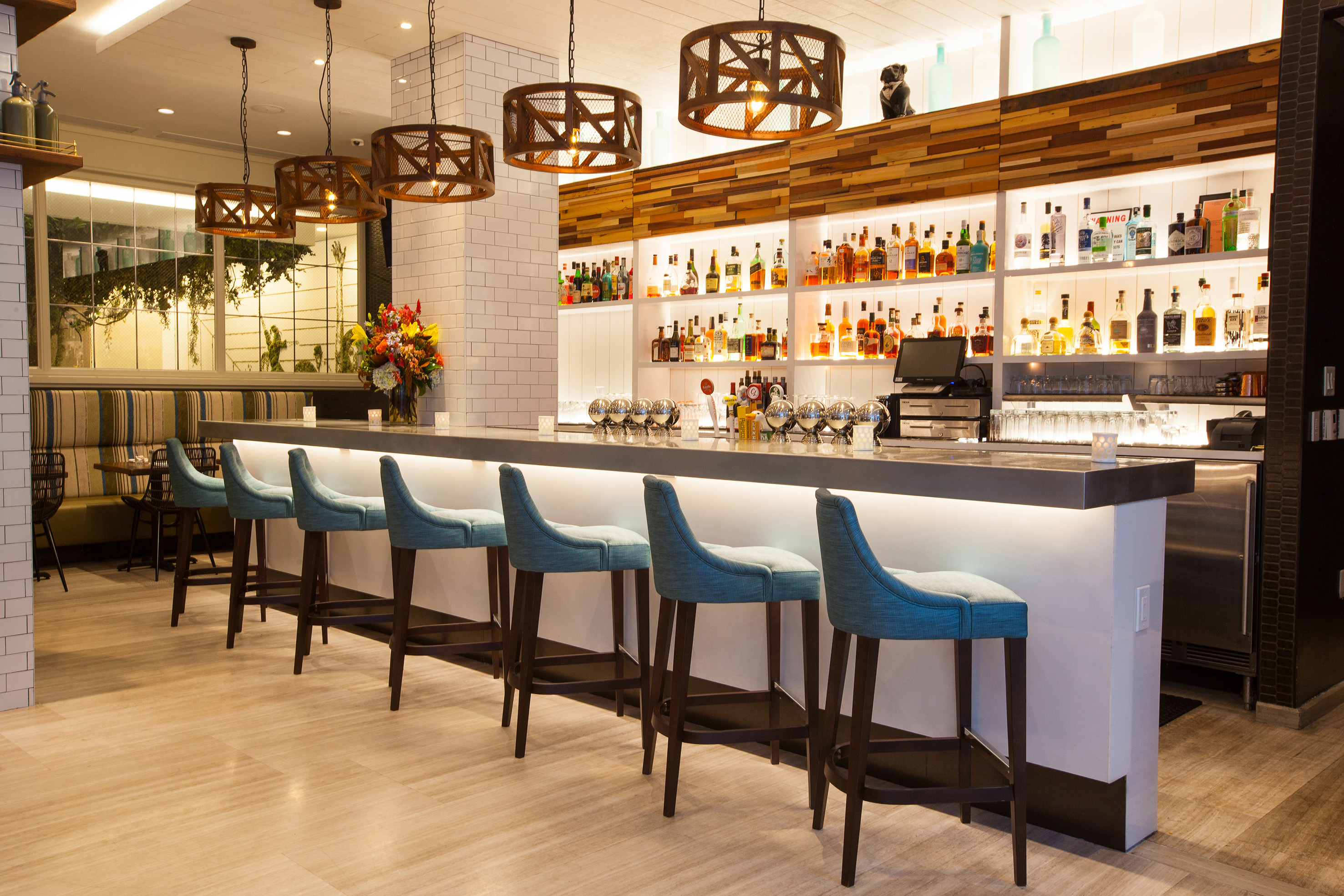 Modern bar with teal bar stools, illuminated liquor shelves, and rustic pendants.