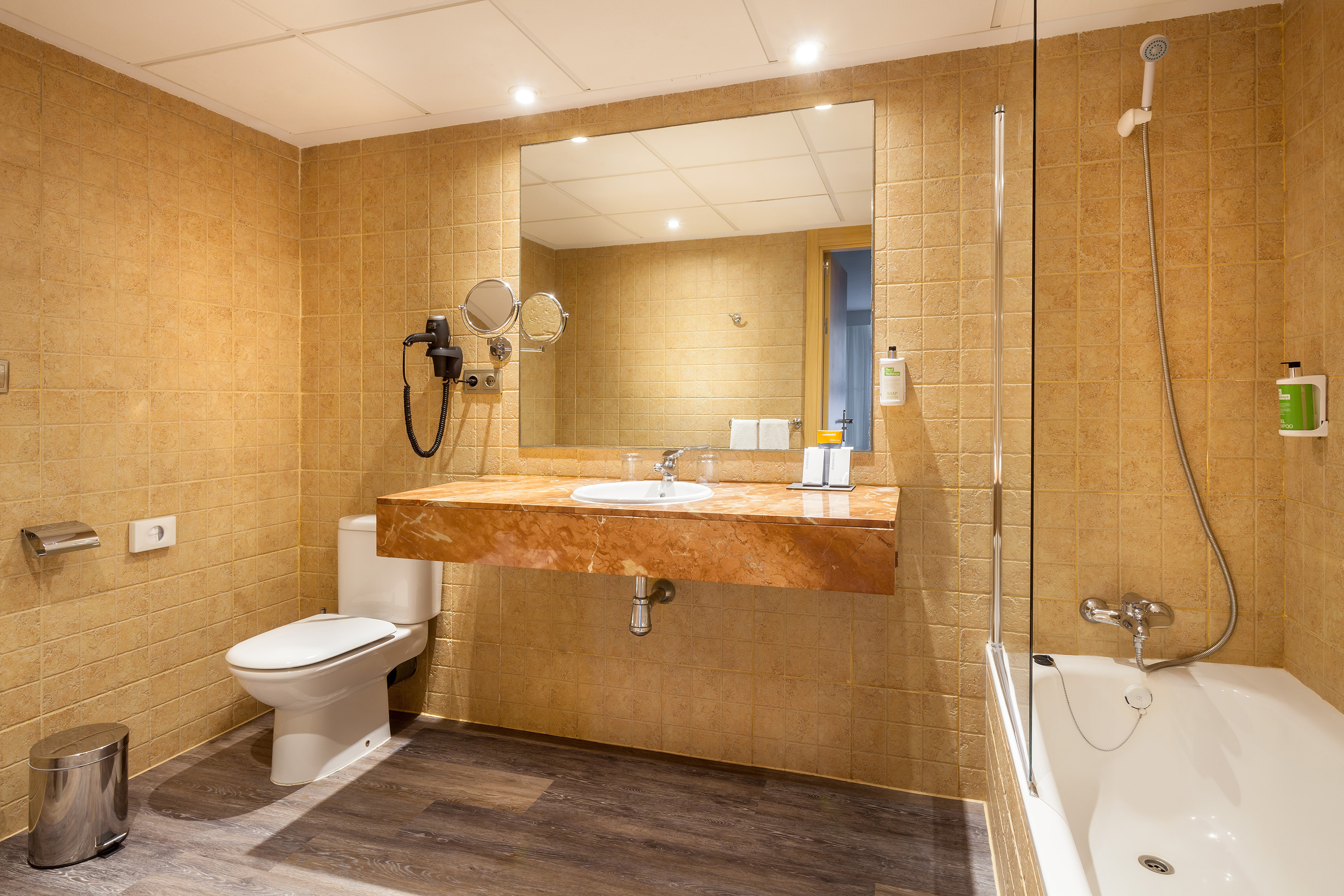 Beige tiled hotel bathroom with marble vanity, sink, toilet, and shower-bathtub.