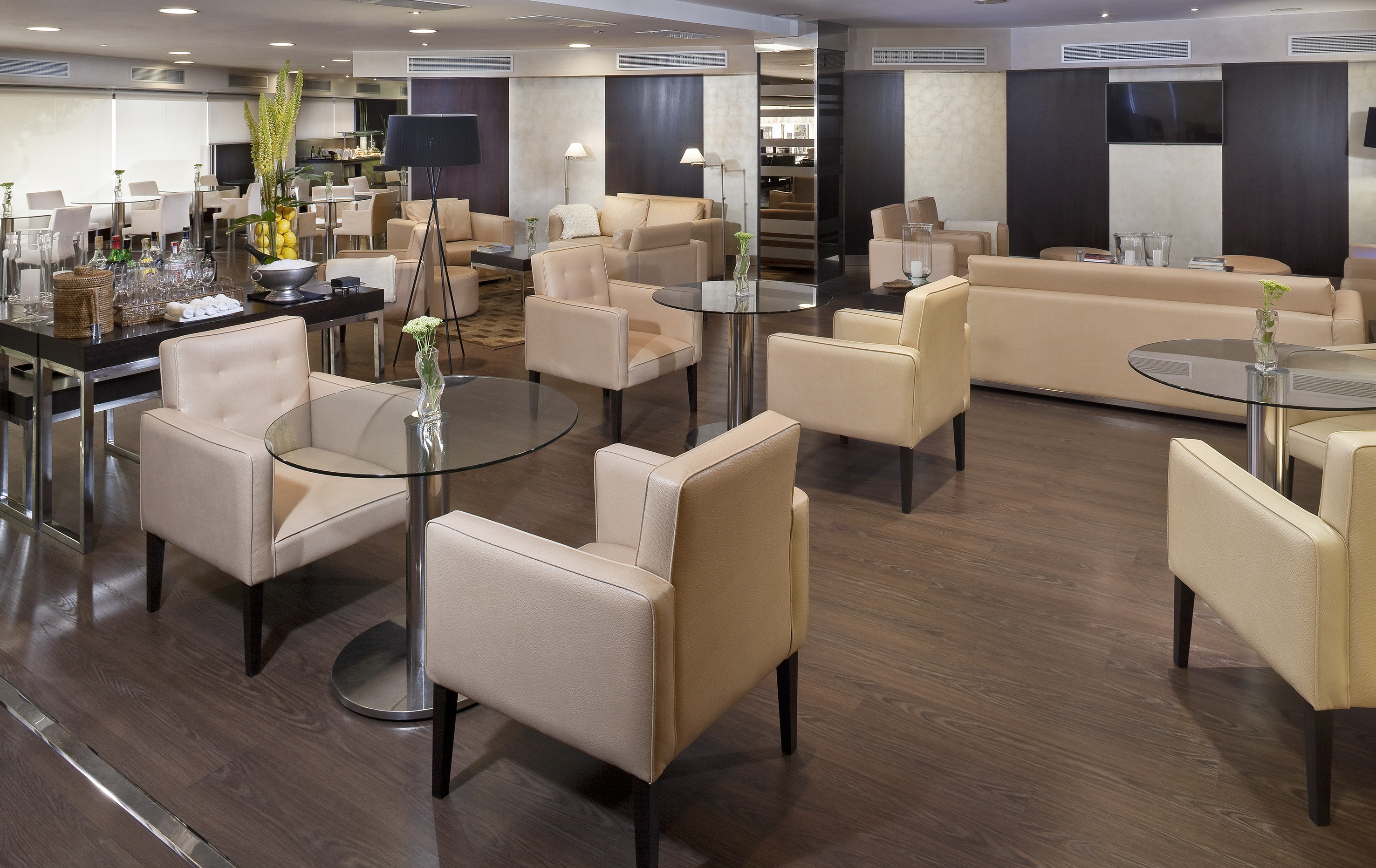 Modern hotel lounge with beige seating, glass tables, and dark wood flooring.