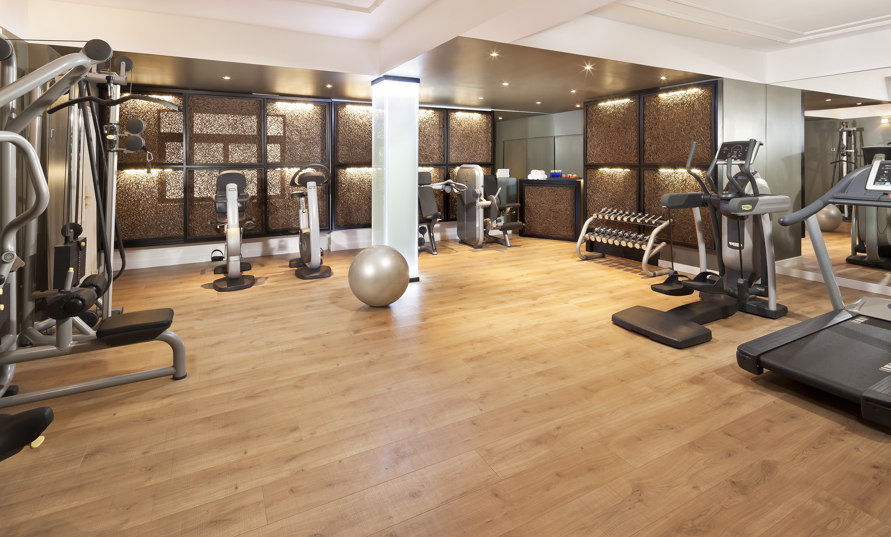 Modern gym with various workout equipment, weights, and wooden floor.