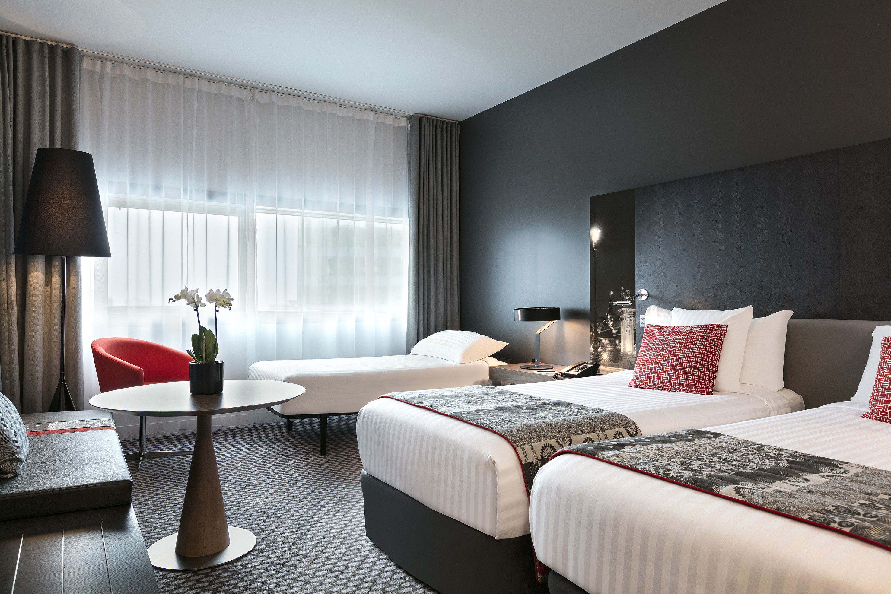 Modern twin hotel room with two beds, an extra bed, and contemporary decor.