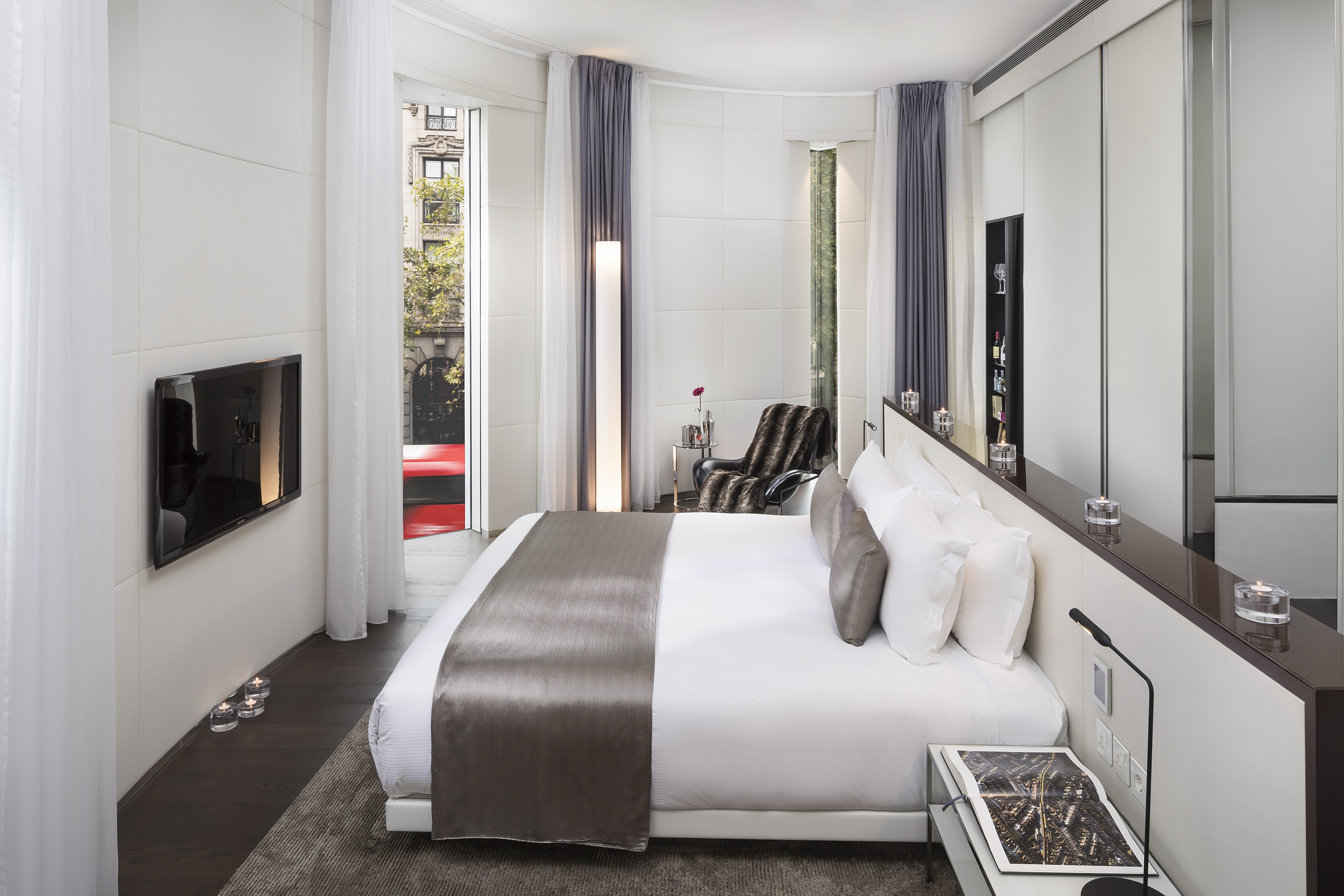 Stylish hotel room featuring a white bed, city view, and sleek modern design.