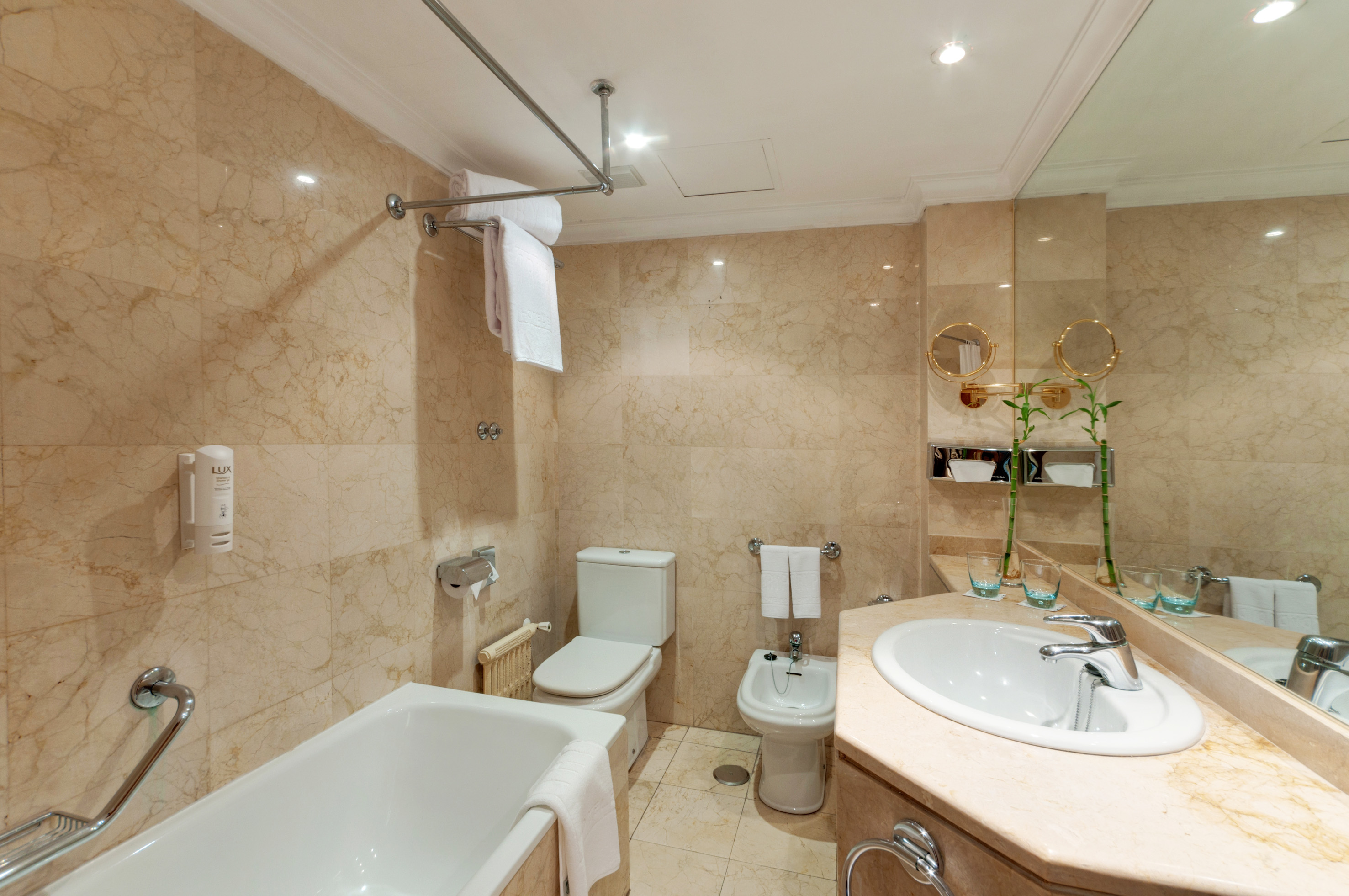 Hotel marble bathroom with bathtub, toilet, bidet, and vanity sink.