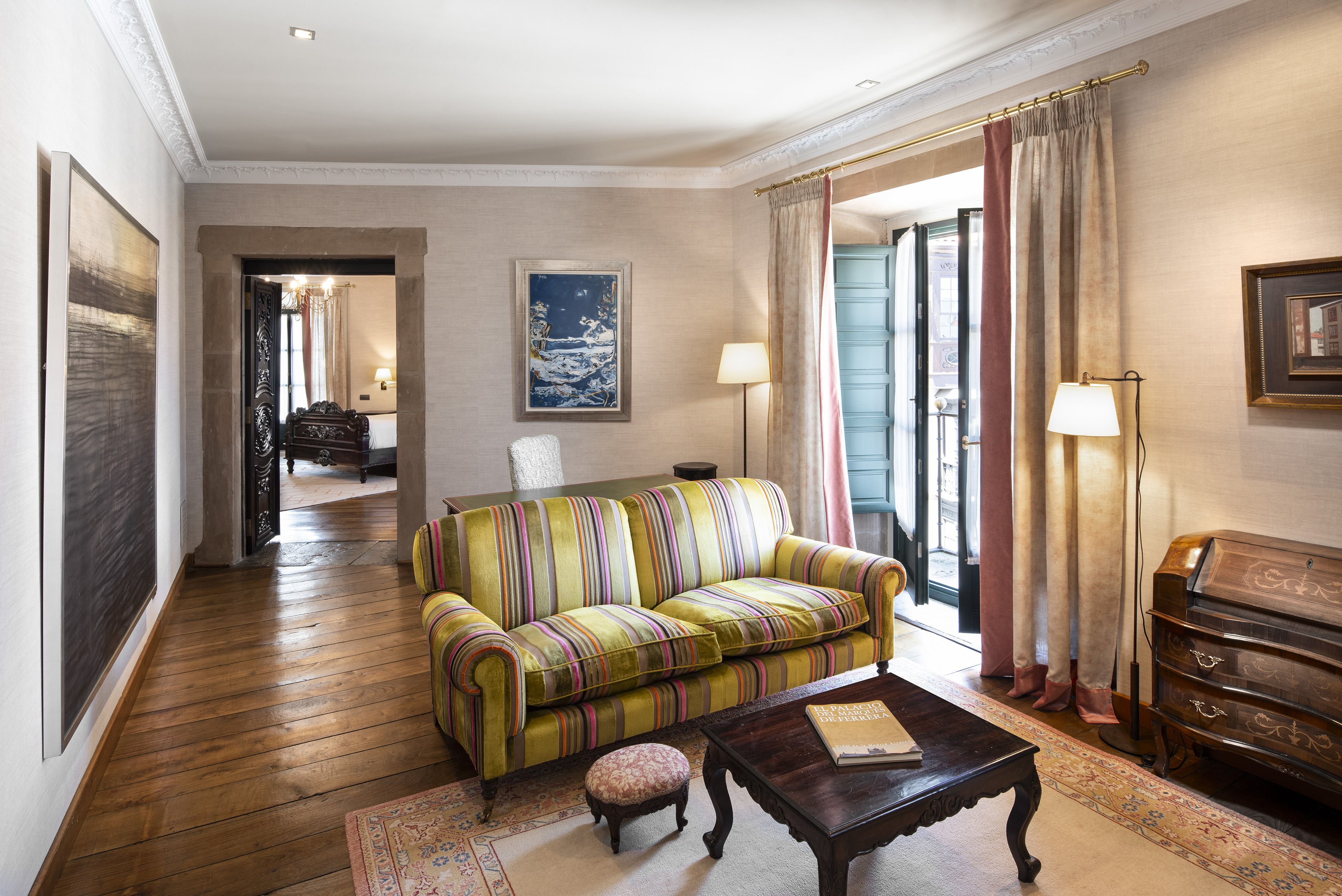 Elegant hotel suite living room with striped sofa, wooden floor, and balcony access.