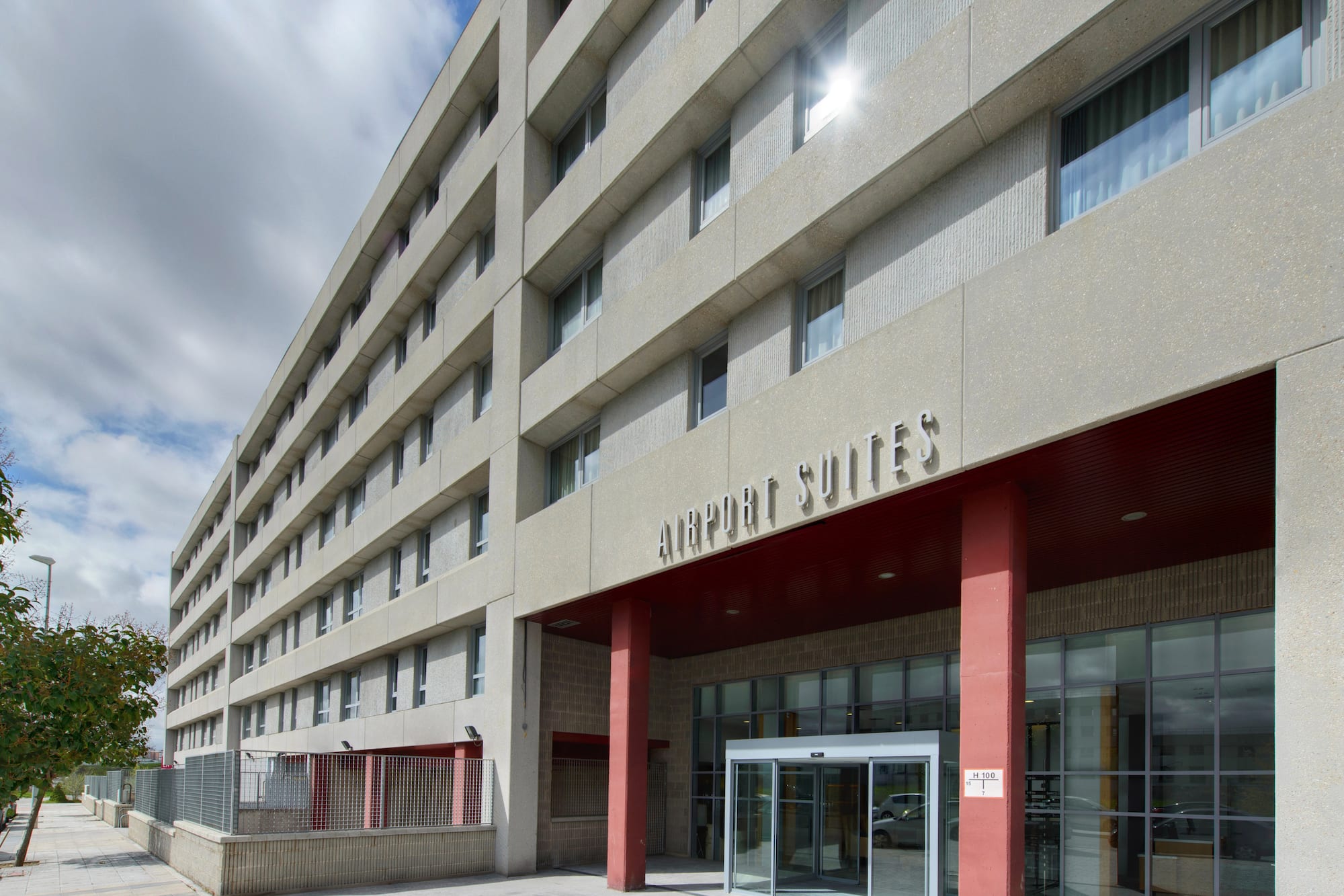 Exterior of Airport Suites hotel, a modern concrete building with red entrance.