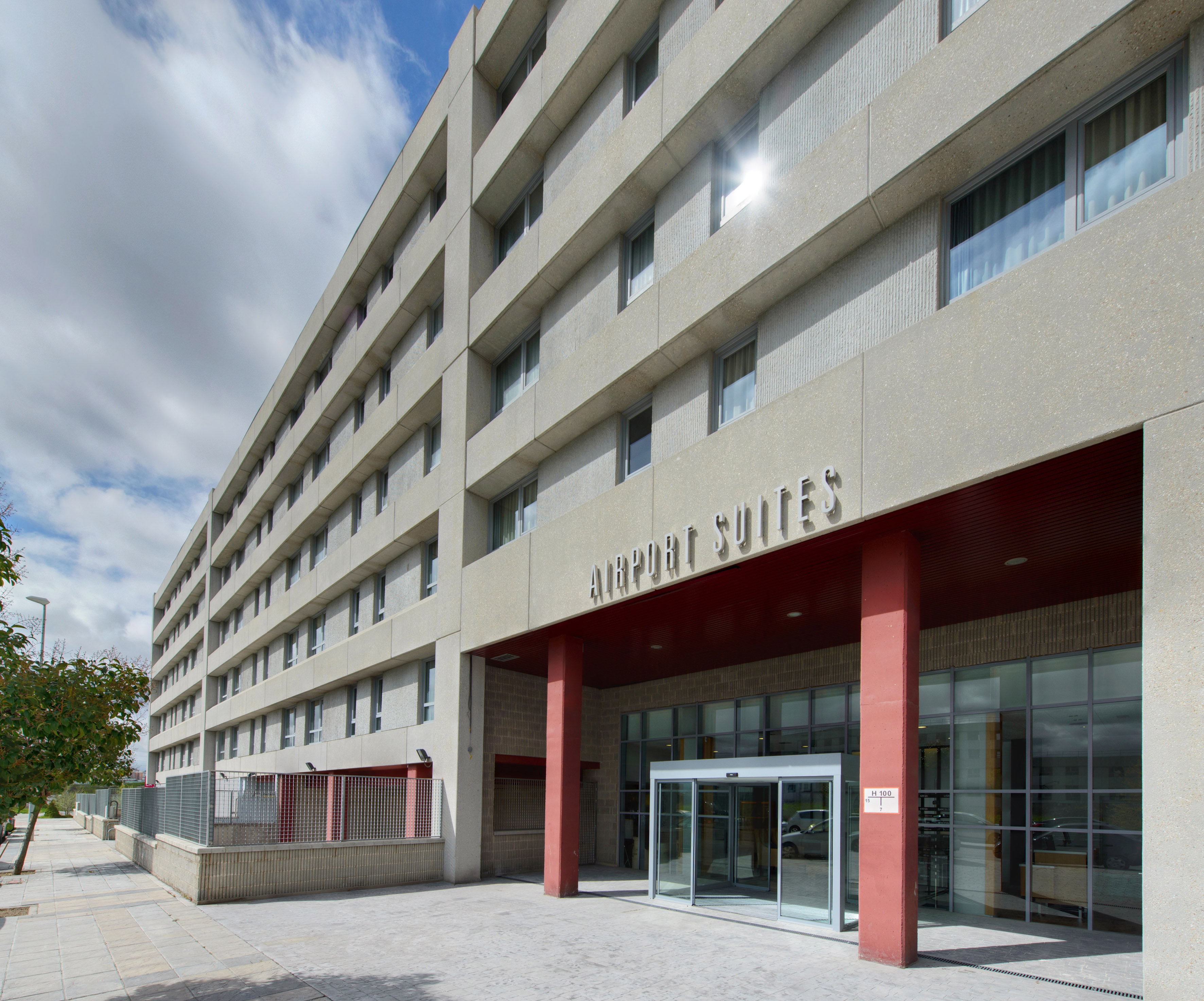 Exterior of Airport Suites hotel, a modern concrete building with red entrance.