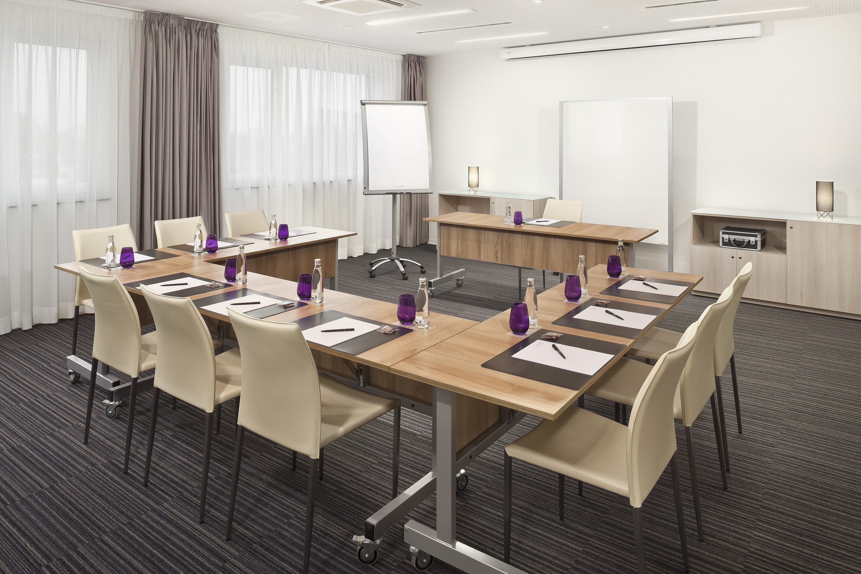 Modern conference room with U-shaped table, beige chairs, flip chart.