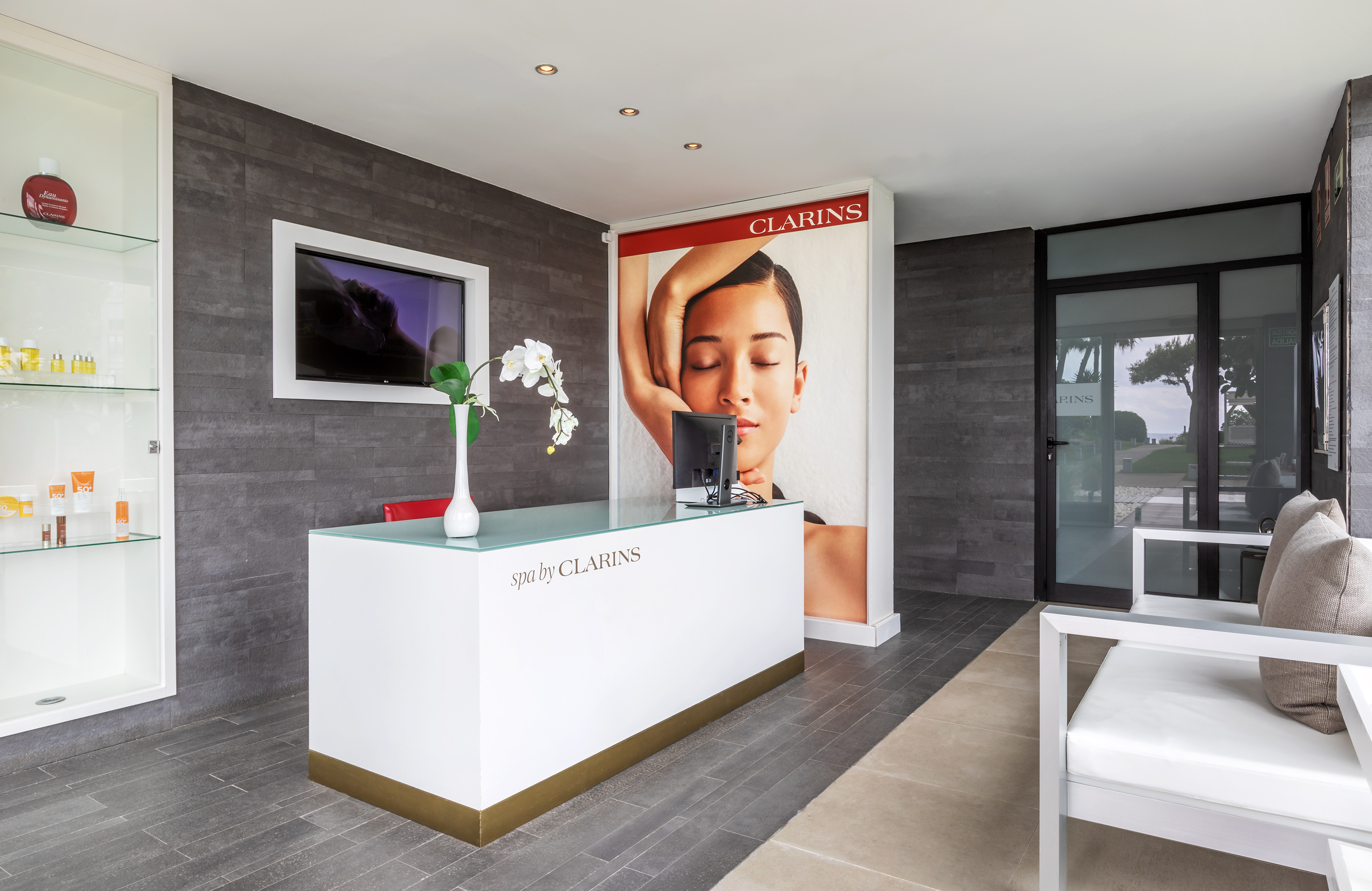Clarins spa reception desk, white counter, beauty products, and modern interior.