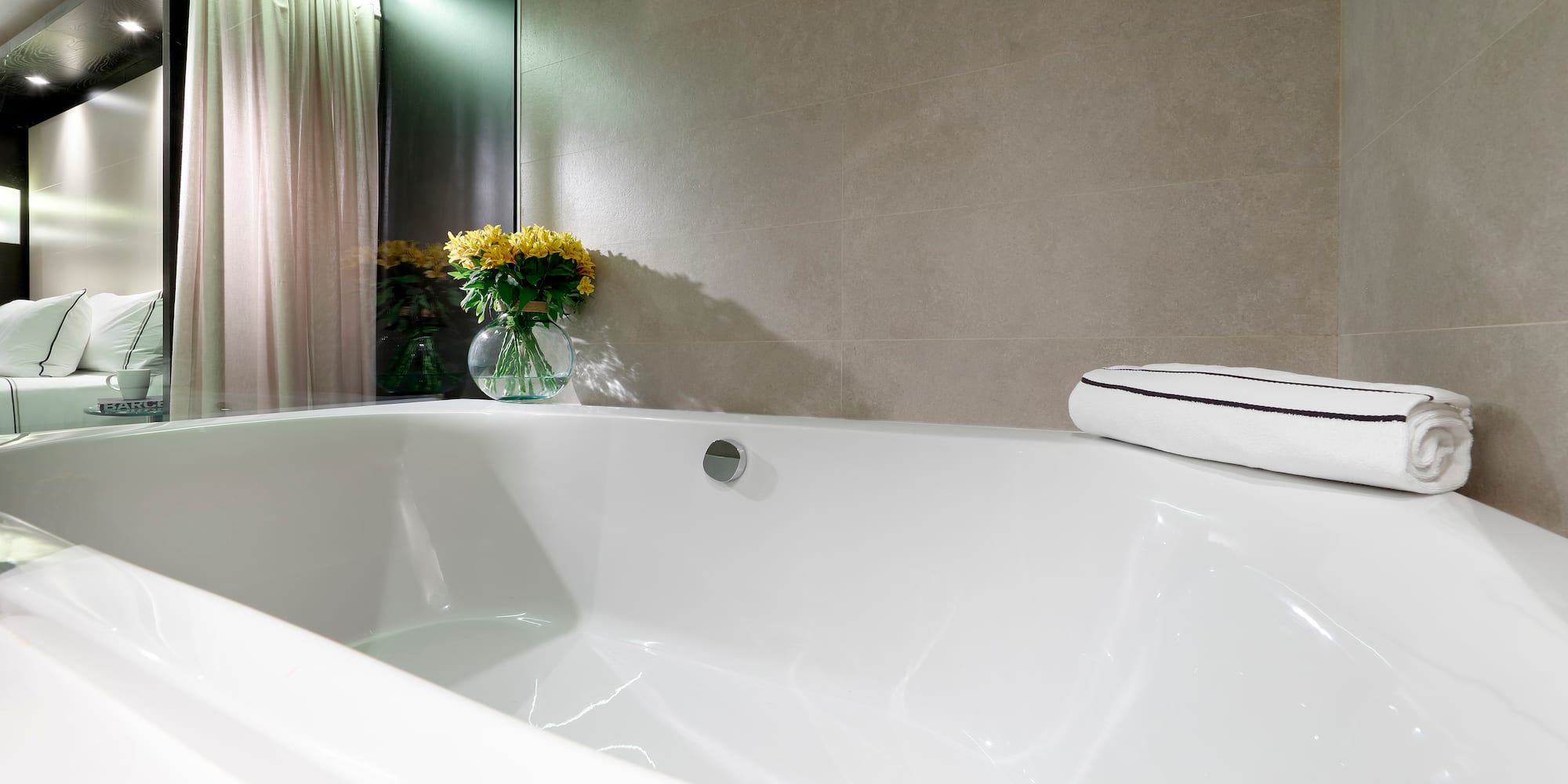 Modern hotel bathroom: white bathtub, grey tiles, yellow flowers.