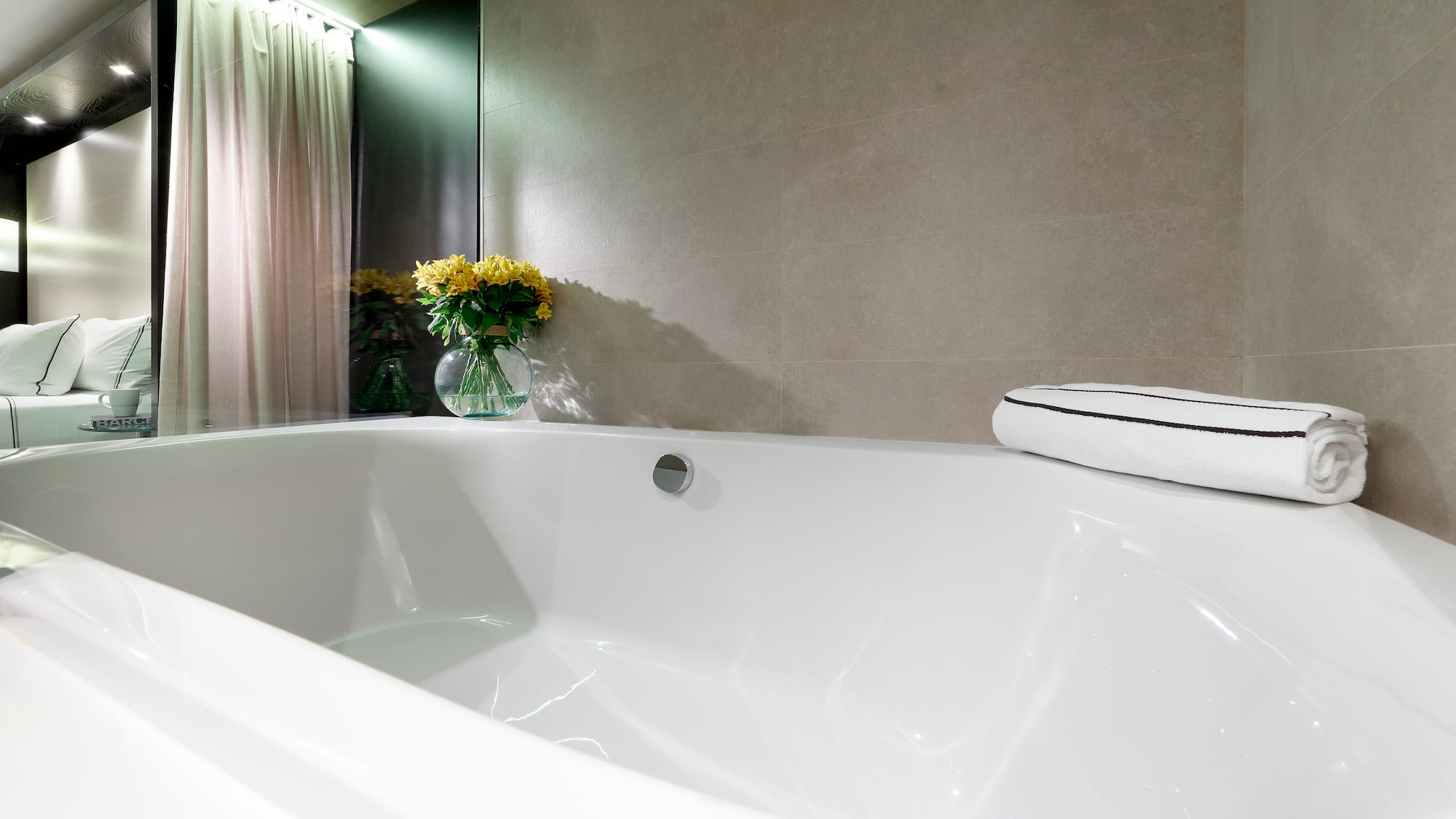 Modern hotel bathroom: white bathtub, grey tiles, yellow flowers.