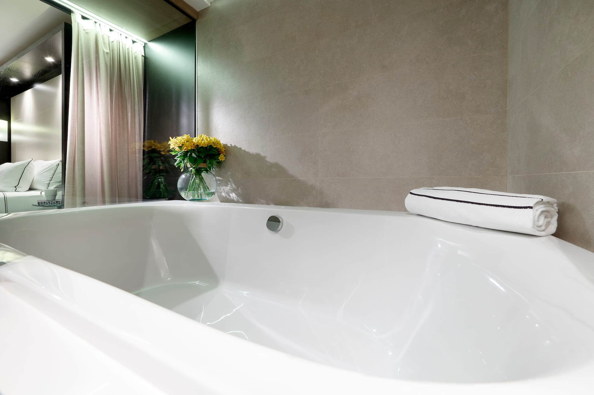 Modern hotel bathroom: white bathtub, grey tiles, yellow flowers.