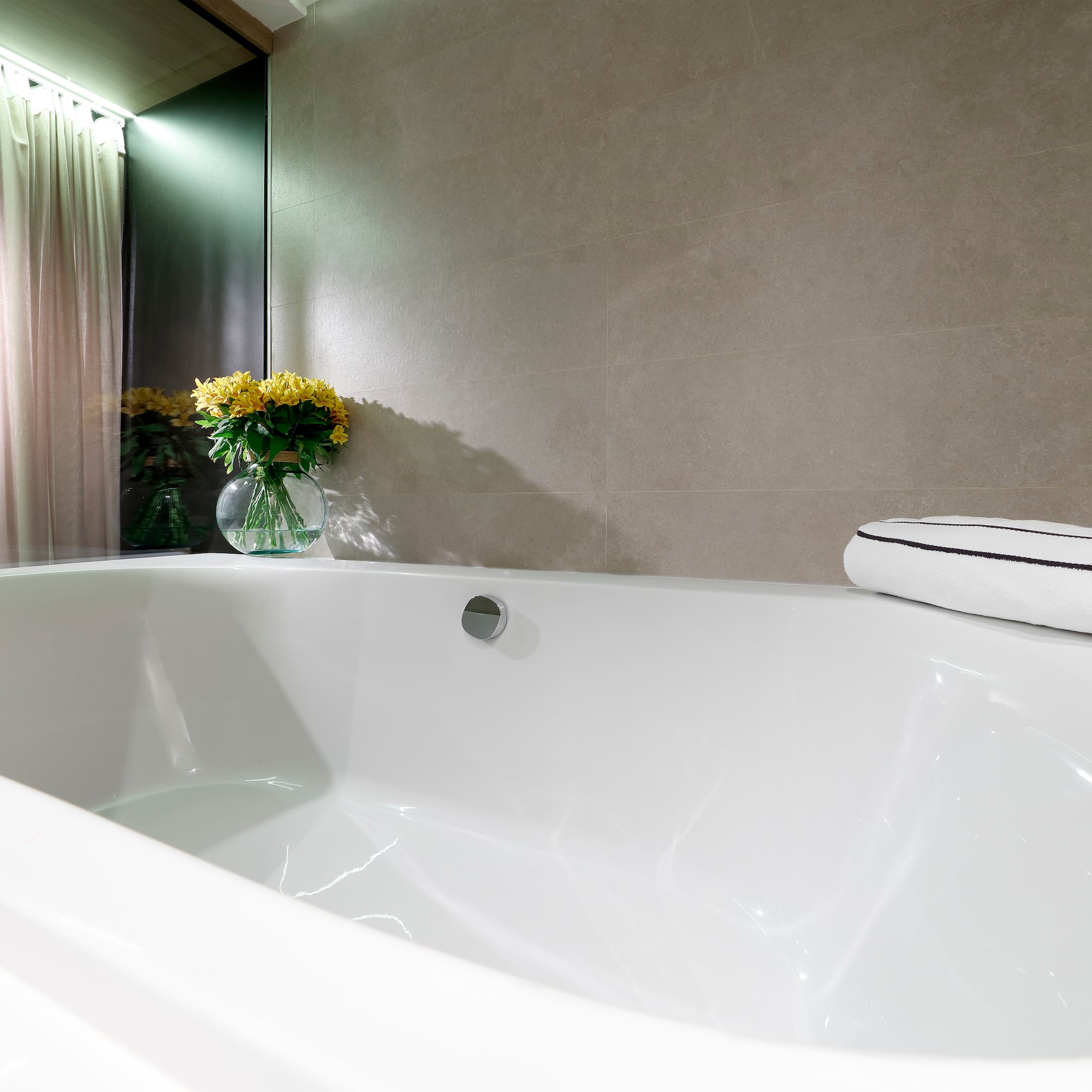 Modern hotel bathroom: white bathtub, grey tiles, yellow flowers.