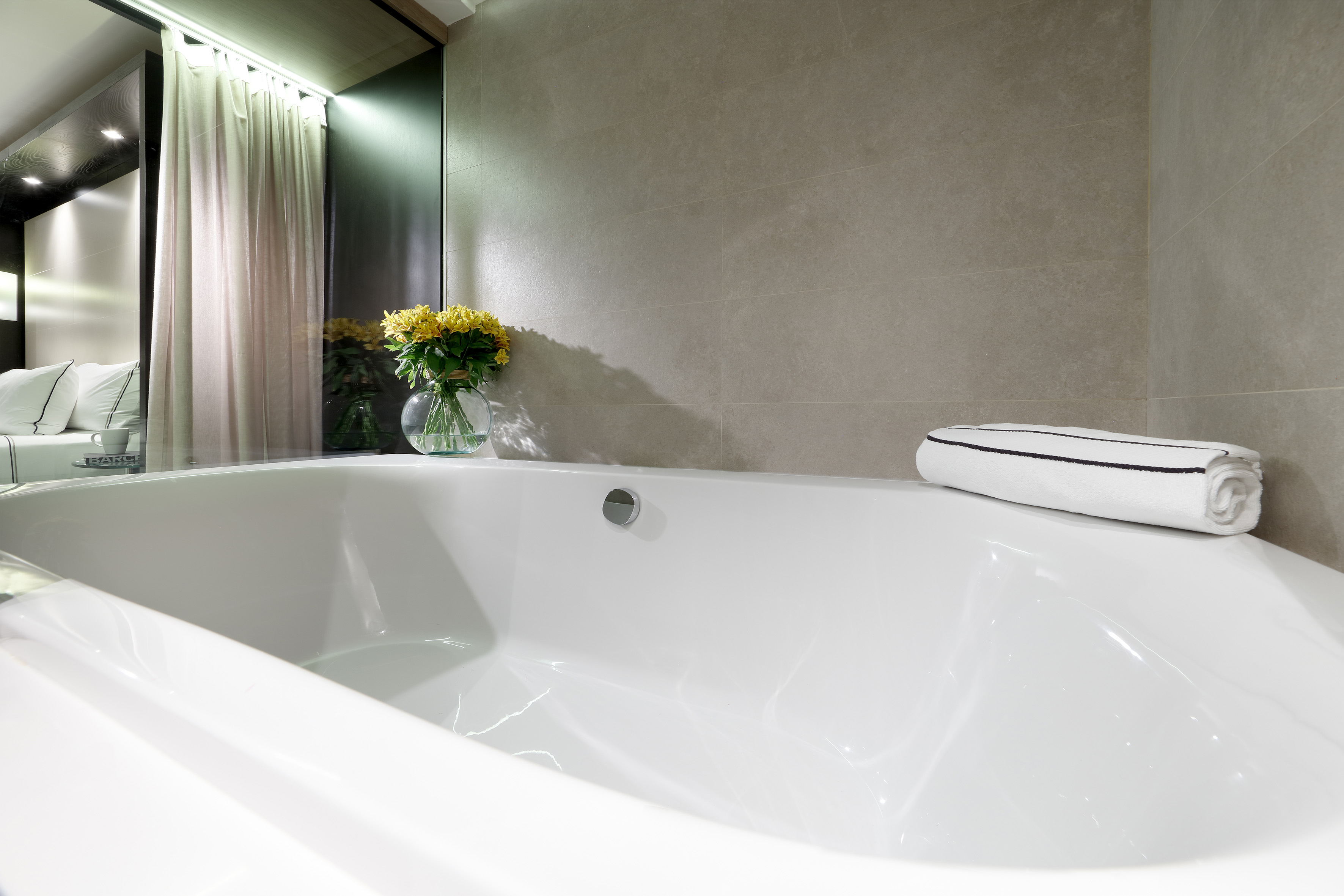 Modern hotel bathroom: white bathtub, grey tiles, yellow flowers.